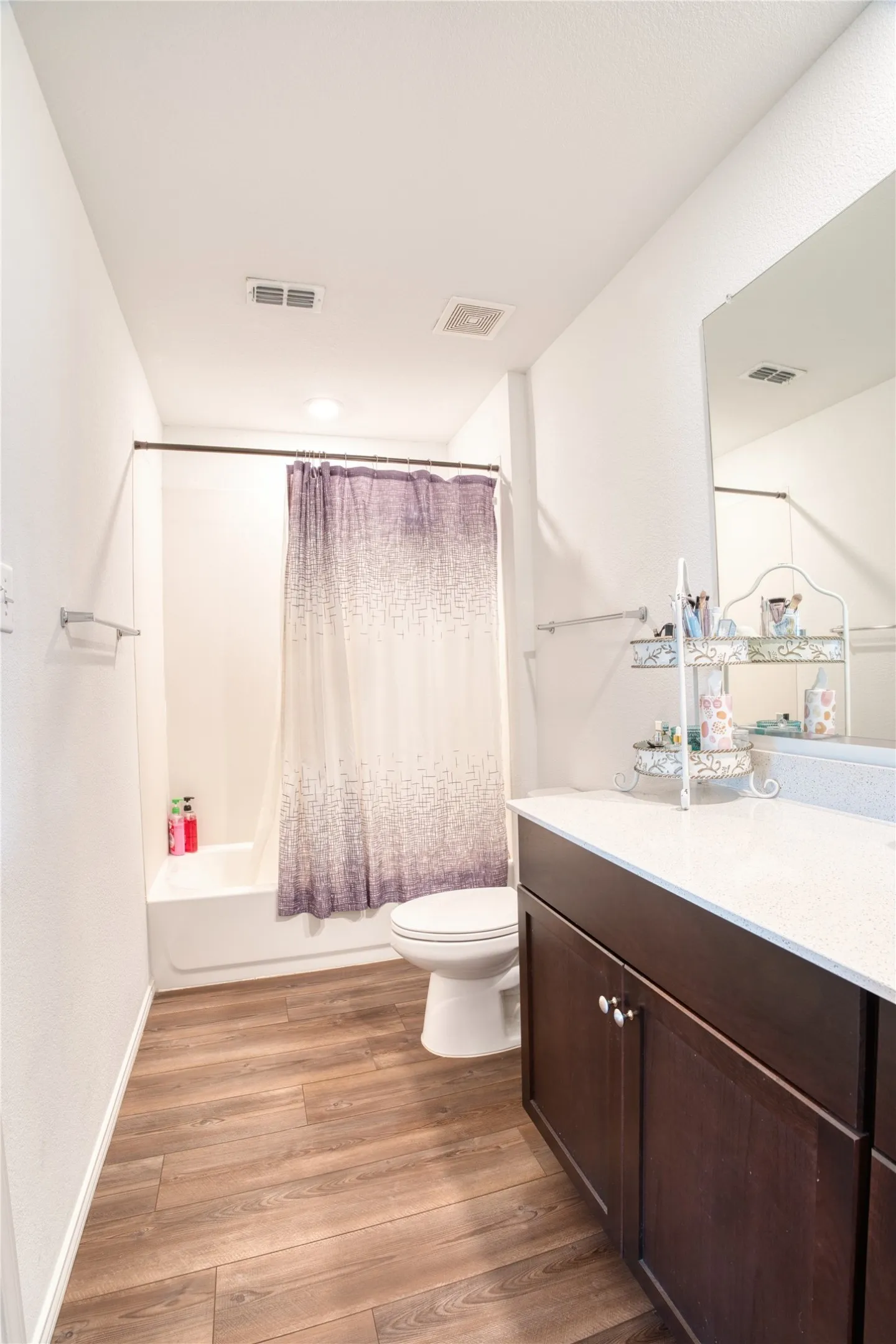 Wood-finish flooring, white walls, built-in vanity with dark wood-finish cabinetry, white countertop, and built-in bathtub with shower