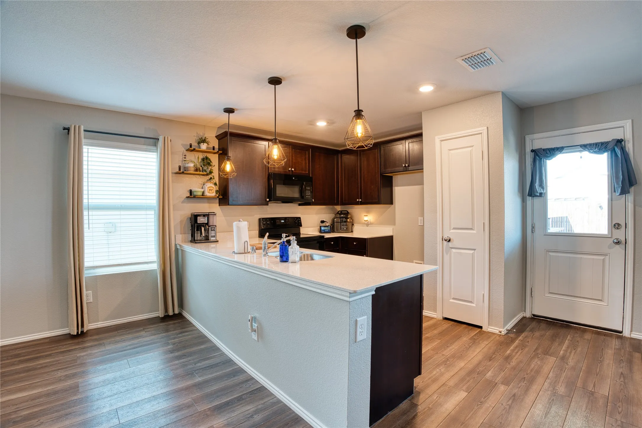 Kitchen featuring a central island with a light-toned countertop, dark wood-finish cabinetry, built-in microwave, wood-finish flooring, and recessed lighting