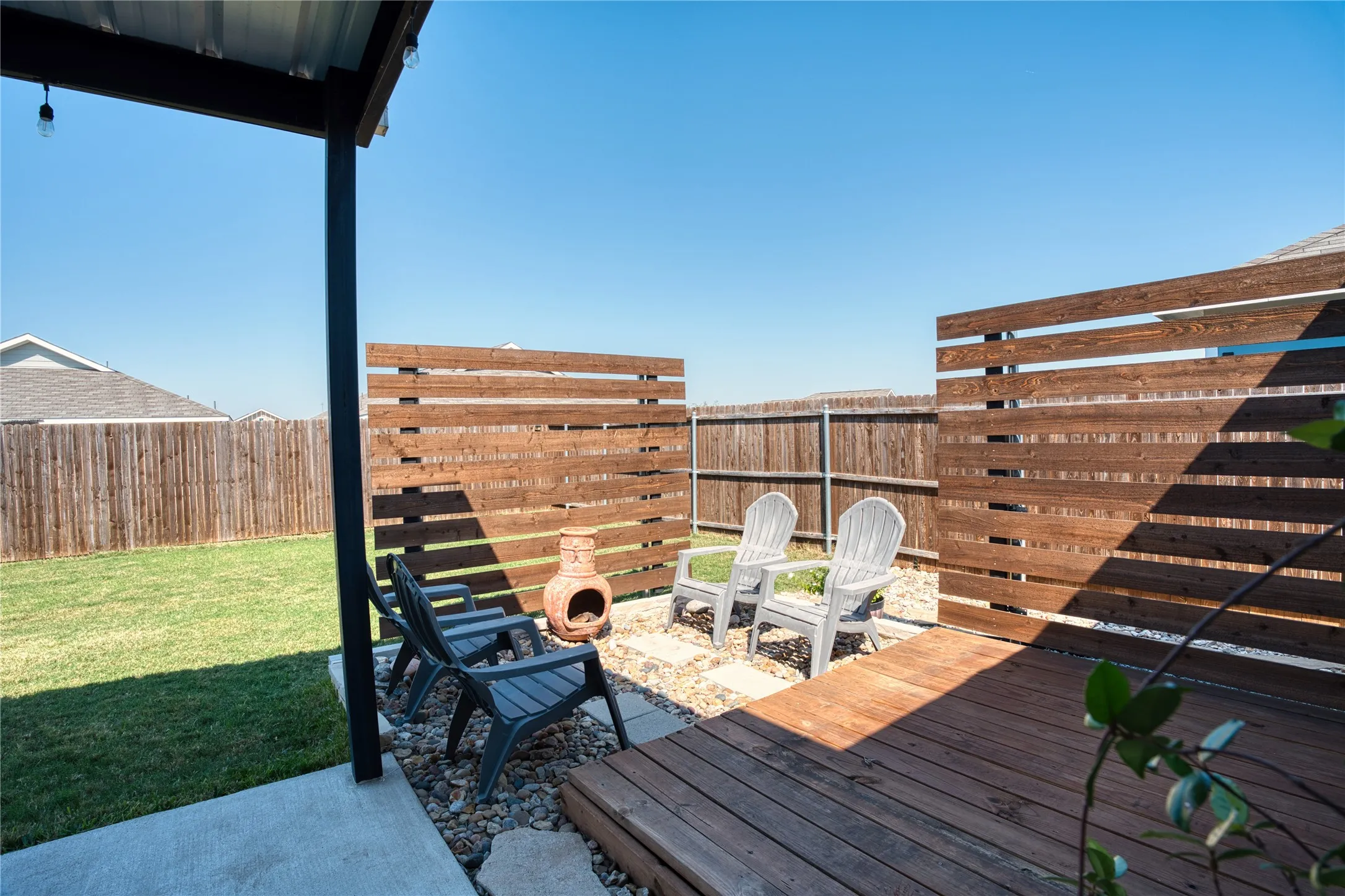 Covered concrete patio with a wood-plank deck, gravel landscaping, and a horizontal slat privacy fence