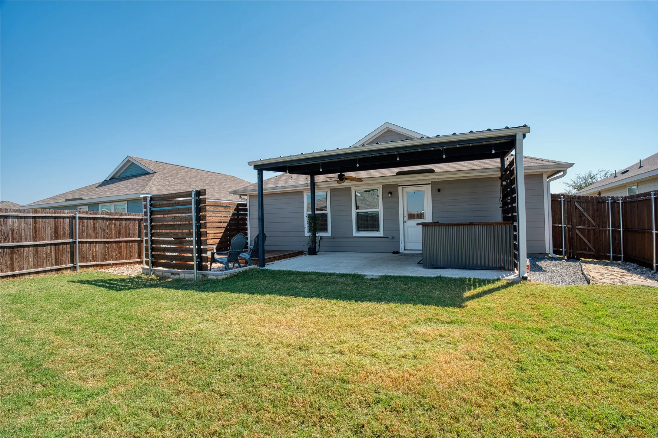 Expansive backyard featuring a concrete patio, a covered pergola with a ceiling fan, and a wood privacy fence