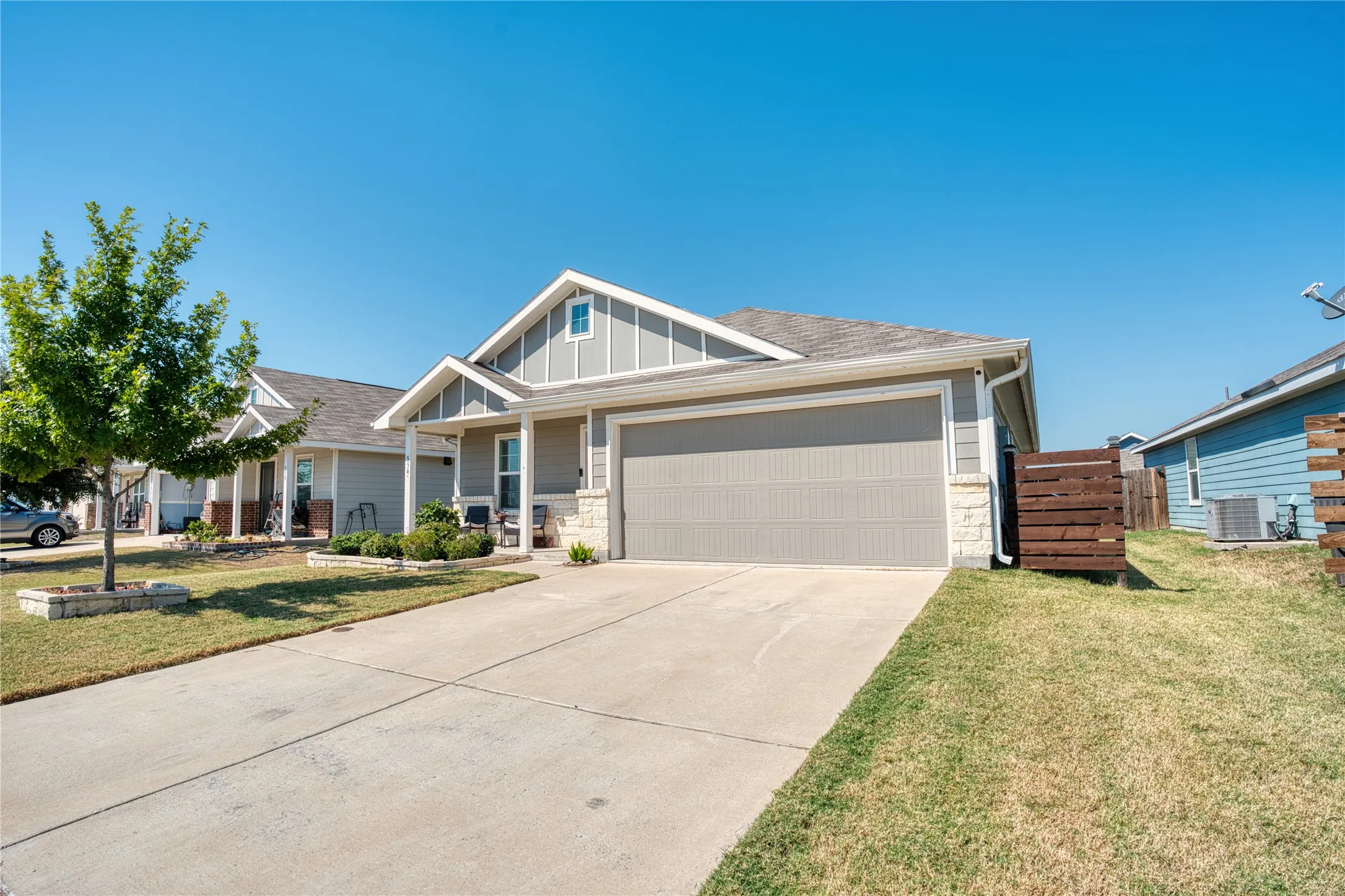 Attached two-car garage with a concrete driveway, a covered front porch, and a stone accent facade
