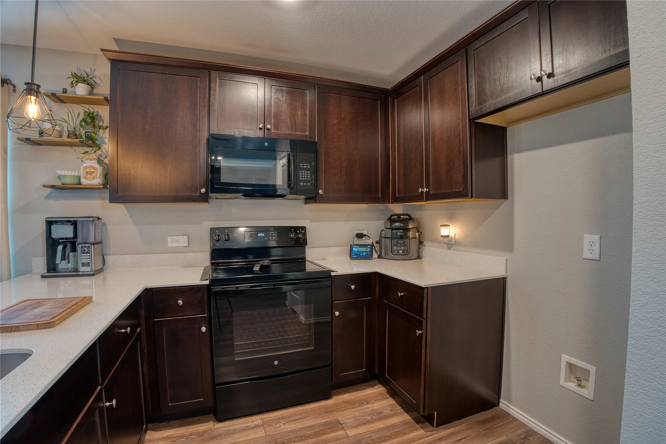 Dark wood-finish cabinetry, light-toned countertops, wood-finish flooring, built-in microwave, and an electric range
