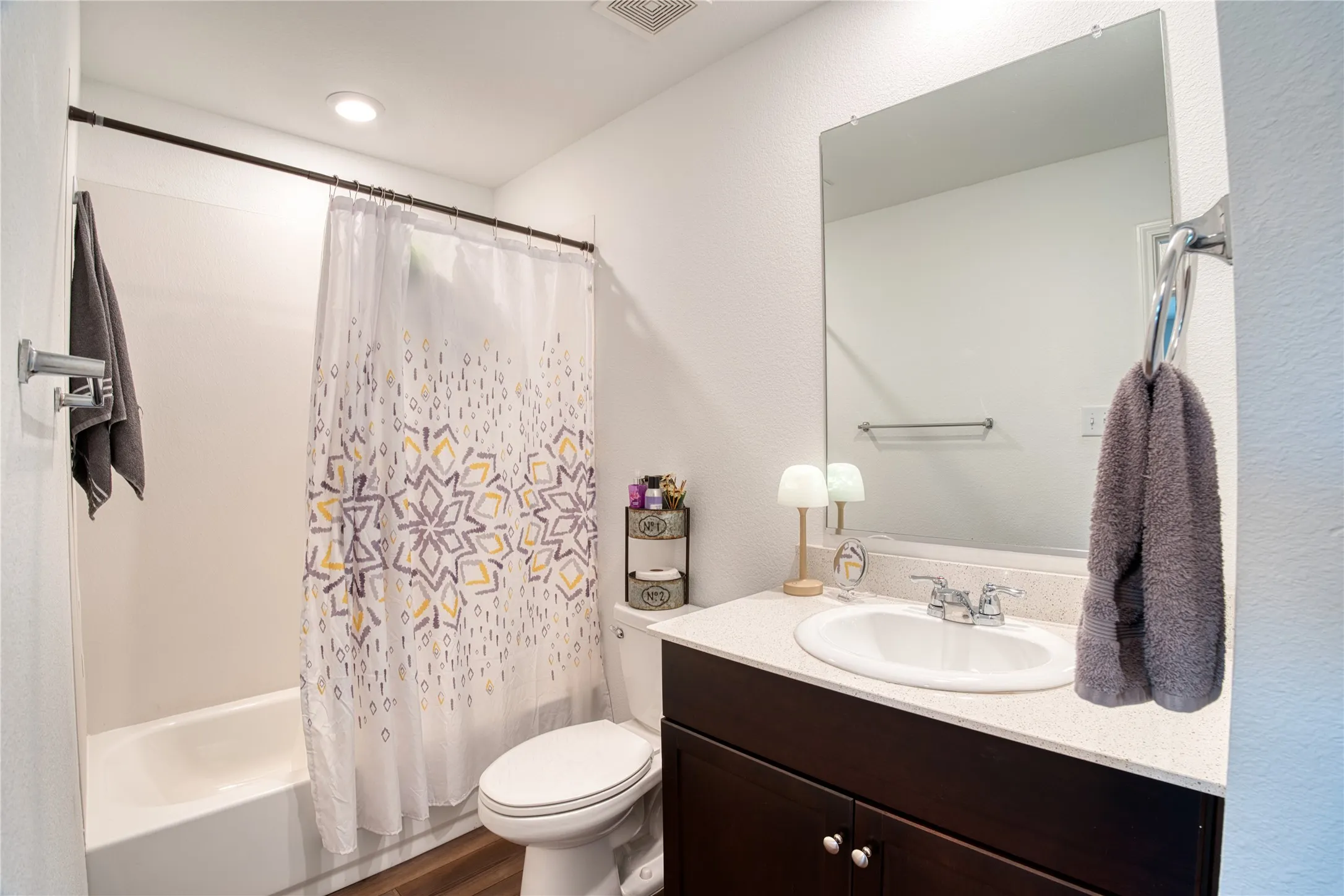 White bathtub with a shower, dark wood-finish vanity with a light-colored countertop, and a wall-mounted mirror
