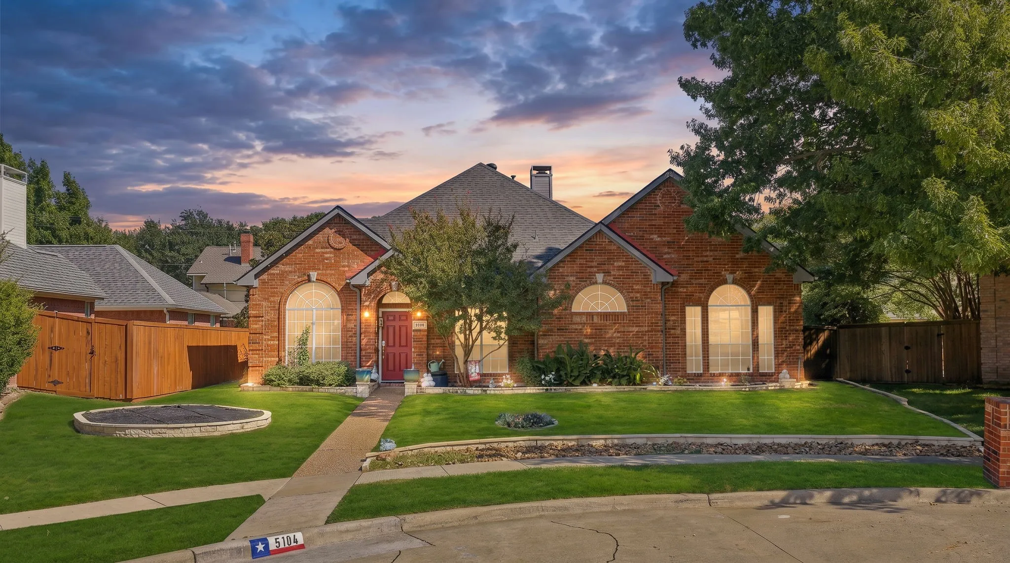Brick exterior with arched windows, a red entry door, a gabled roof, and a stone-edged lawn