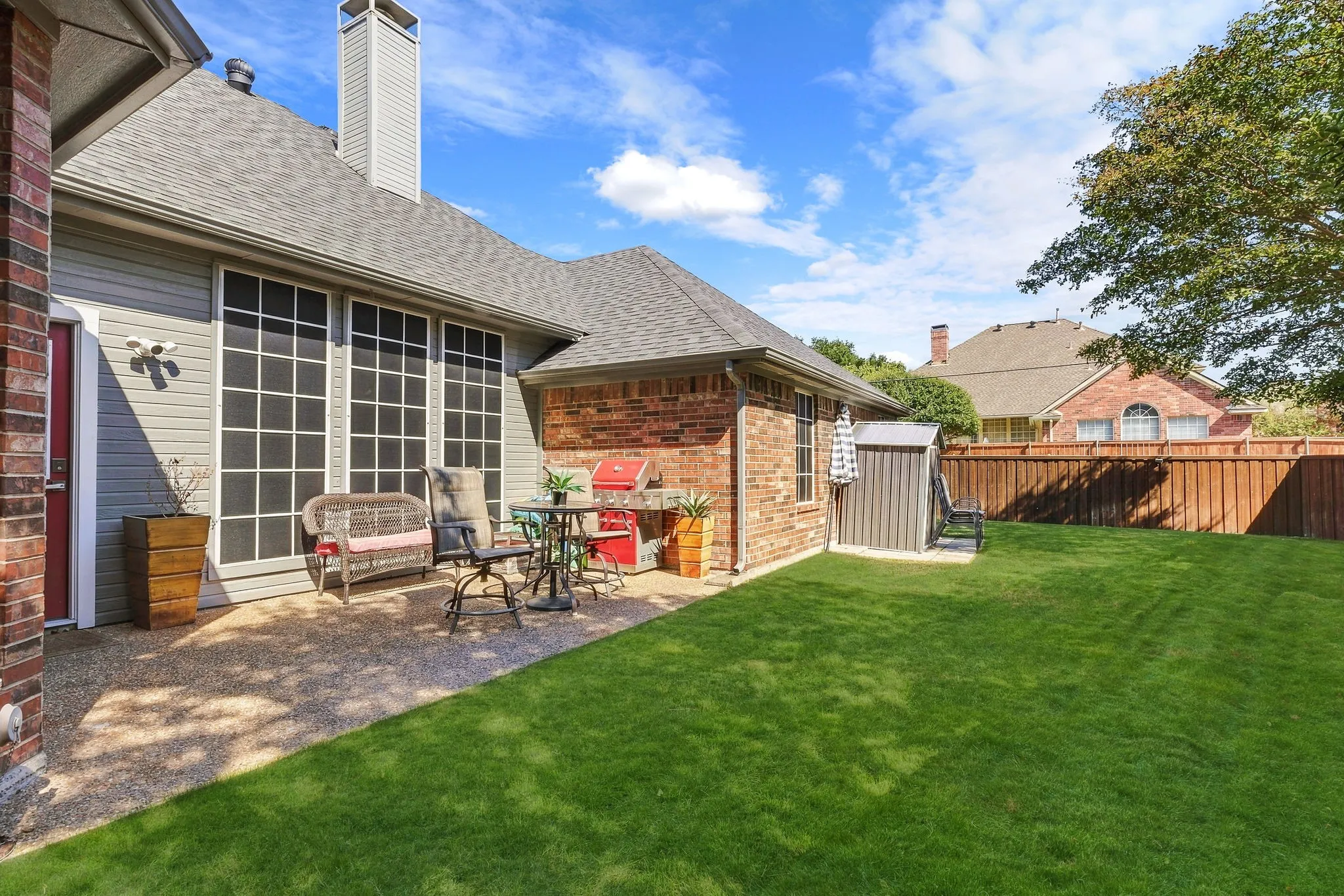 Expansive backyard with a manicured lawn, full privacy fencing, and a stone-finish patio area