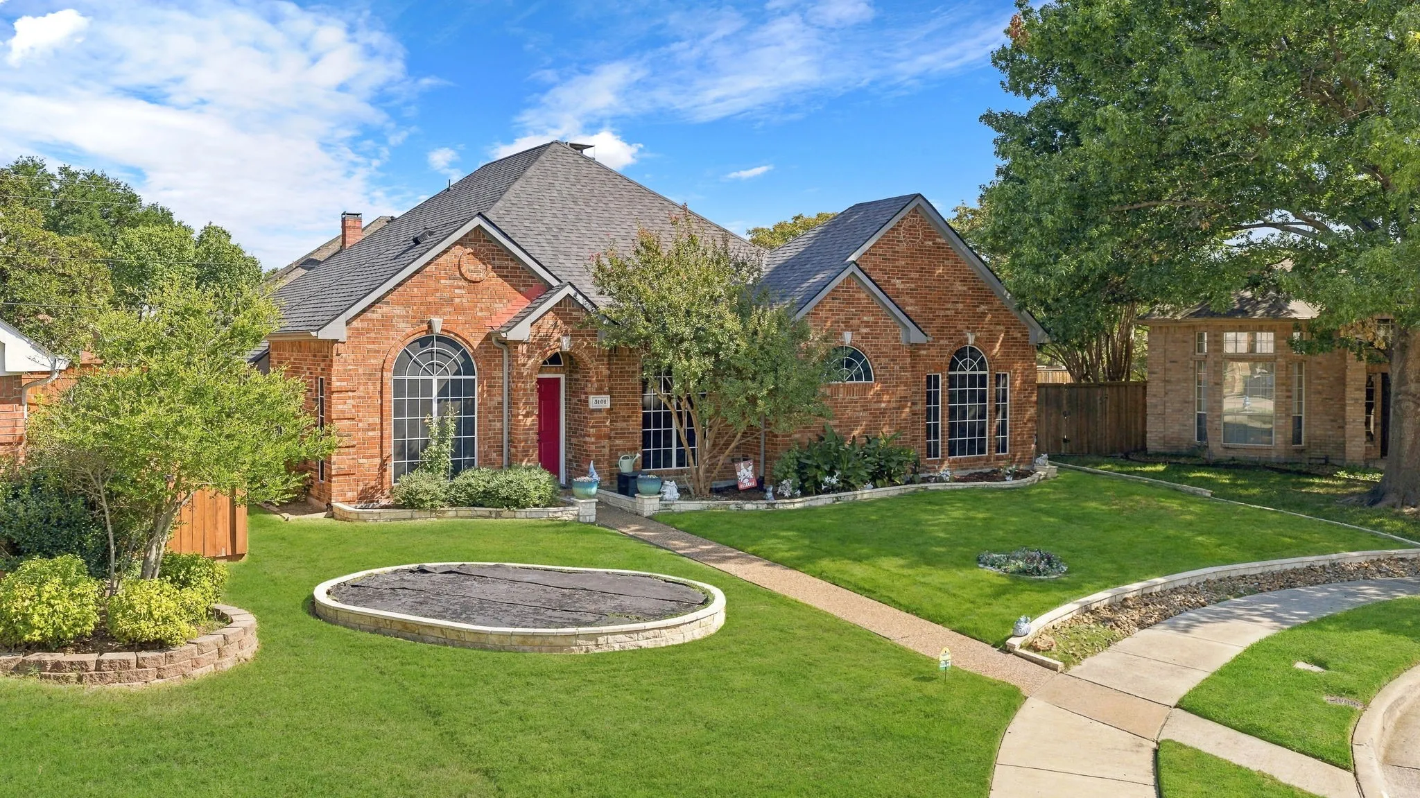Brick exterior with arched windows, dark roofing, and a manicured lawn featuring a circular ground-level element