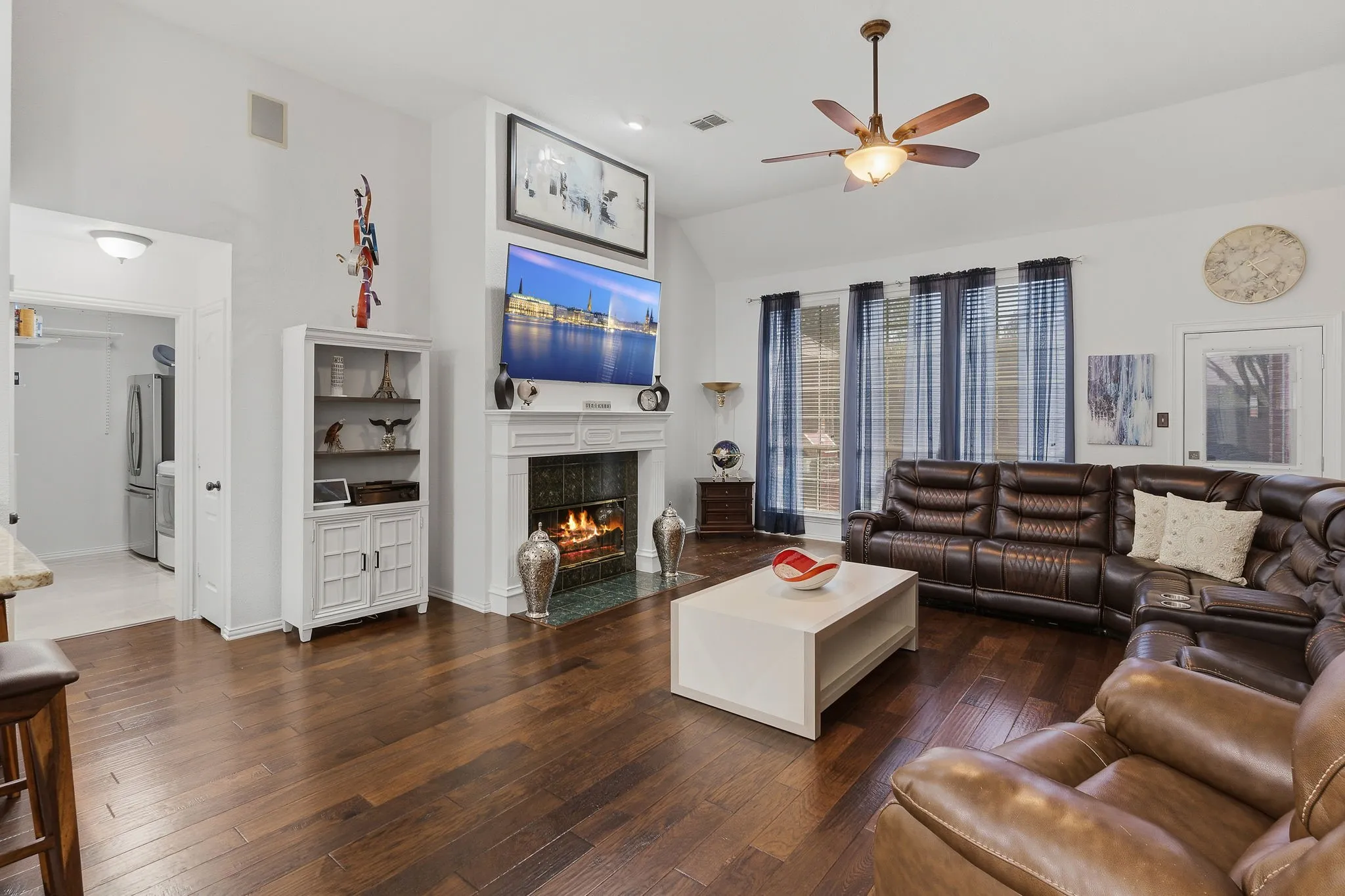 Hardwood-style flooring throughout, vaulted ceiling, and a fireplace with a white mantel and tile surround
