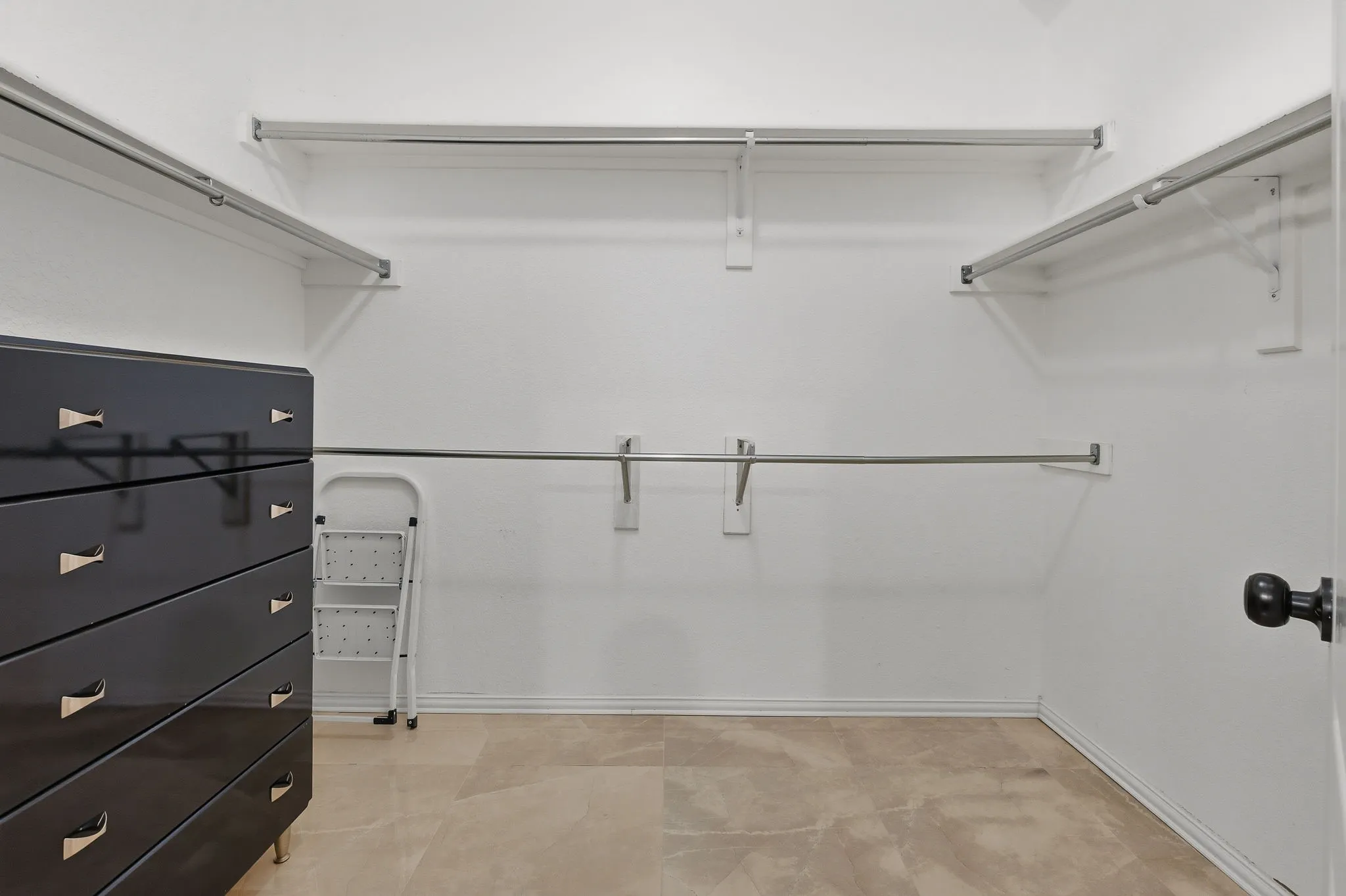 Walk-in closet featuring light-toned flooring, multiple clothing rods, and overhead shelving