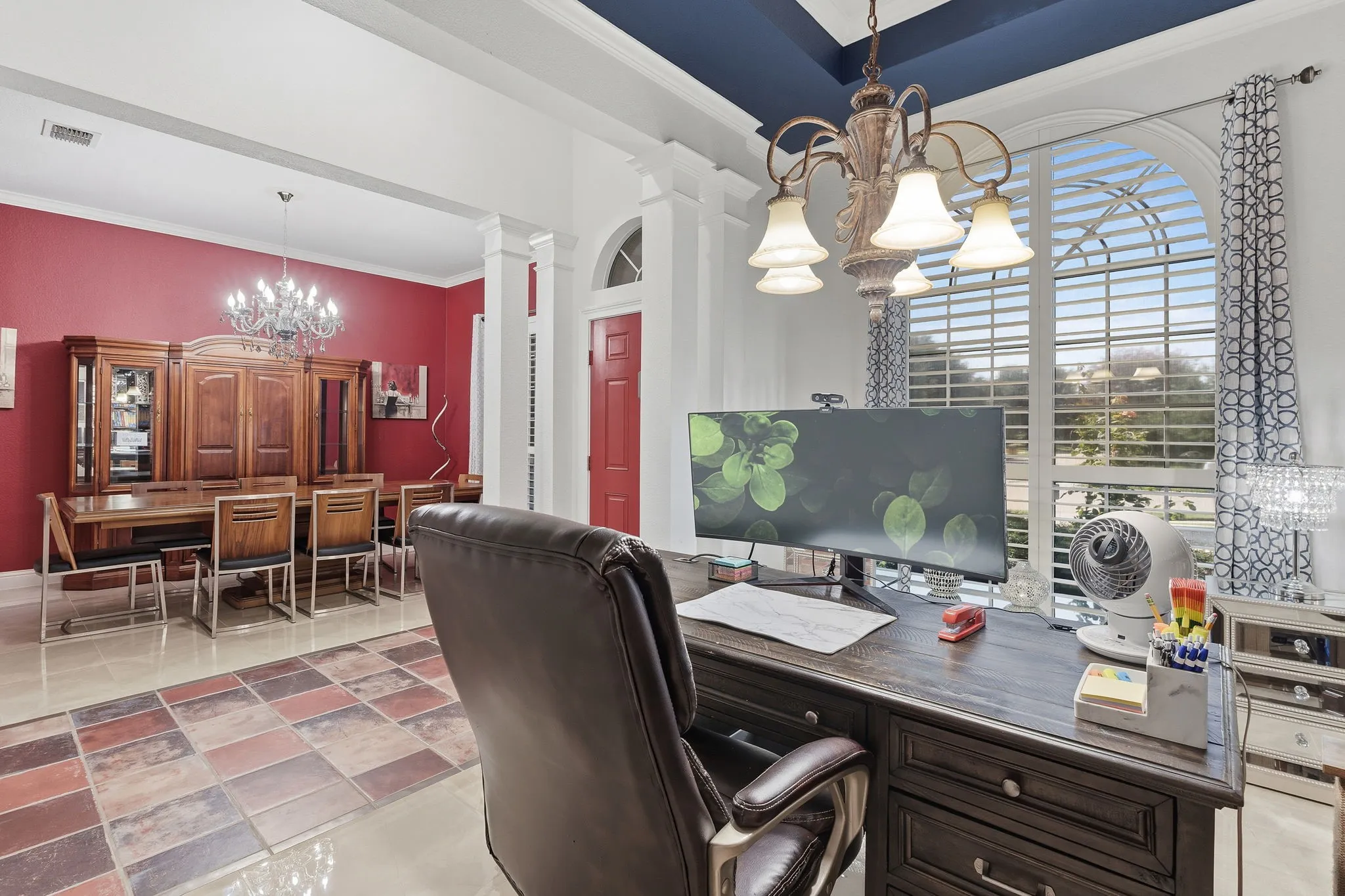 Arched window with plantation shutters, coffered ceiling, chandelier lighting, and a red interior door