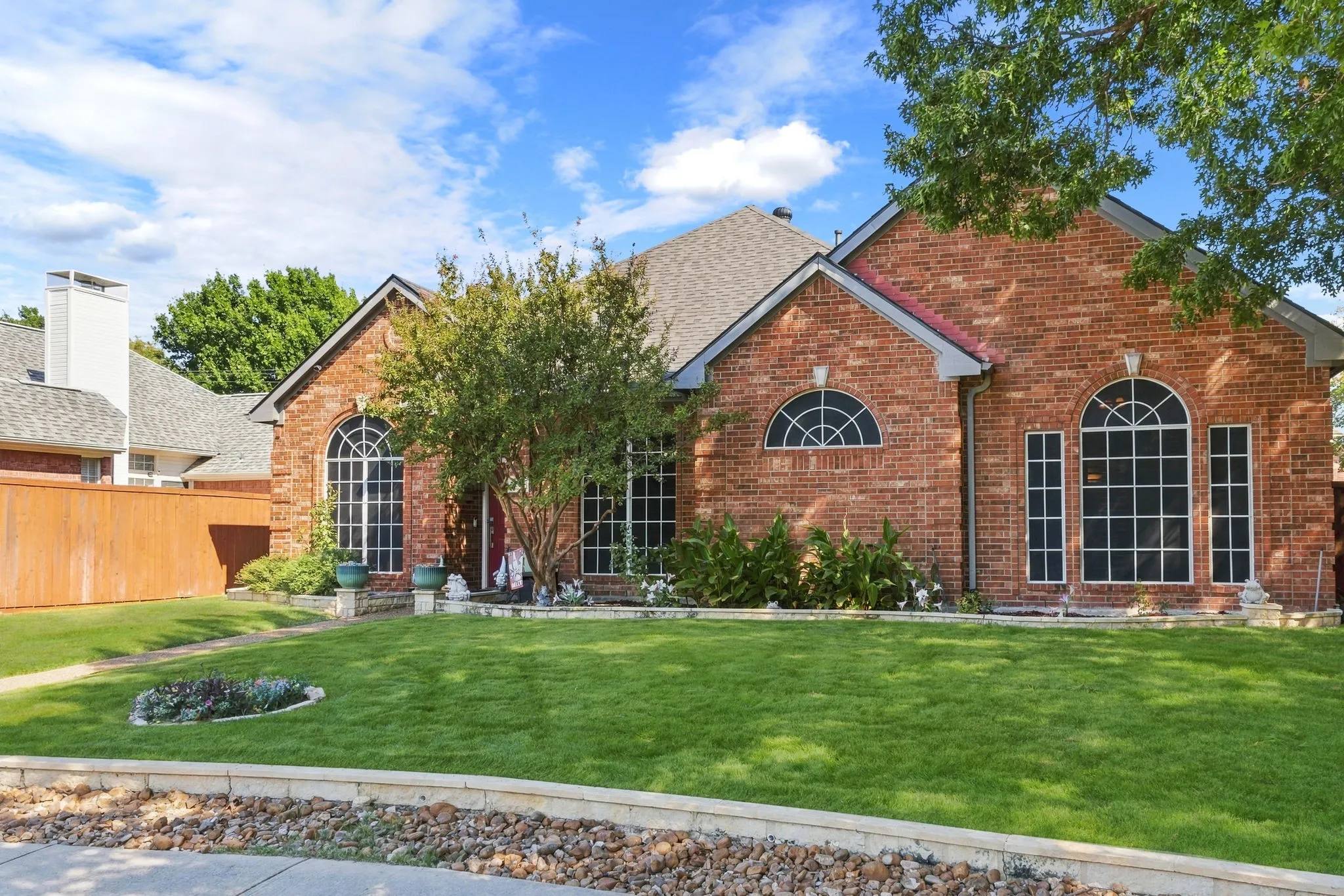 Brick facade with arched windows, gabled roof, and mature landscaping