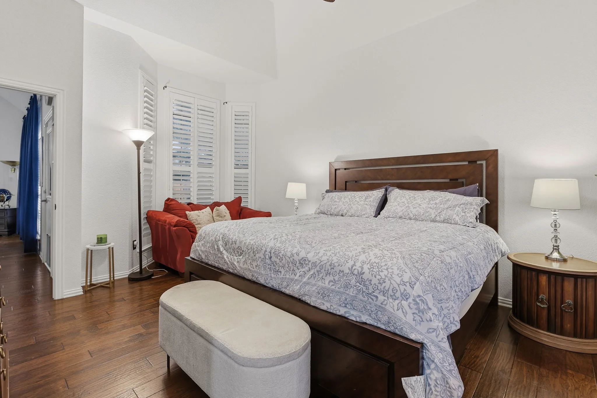 Wood-finish flooring, white walls, angled ceiling, bay window with plantation shutters, and a doorway