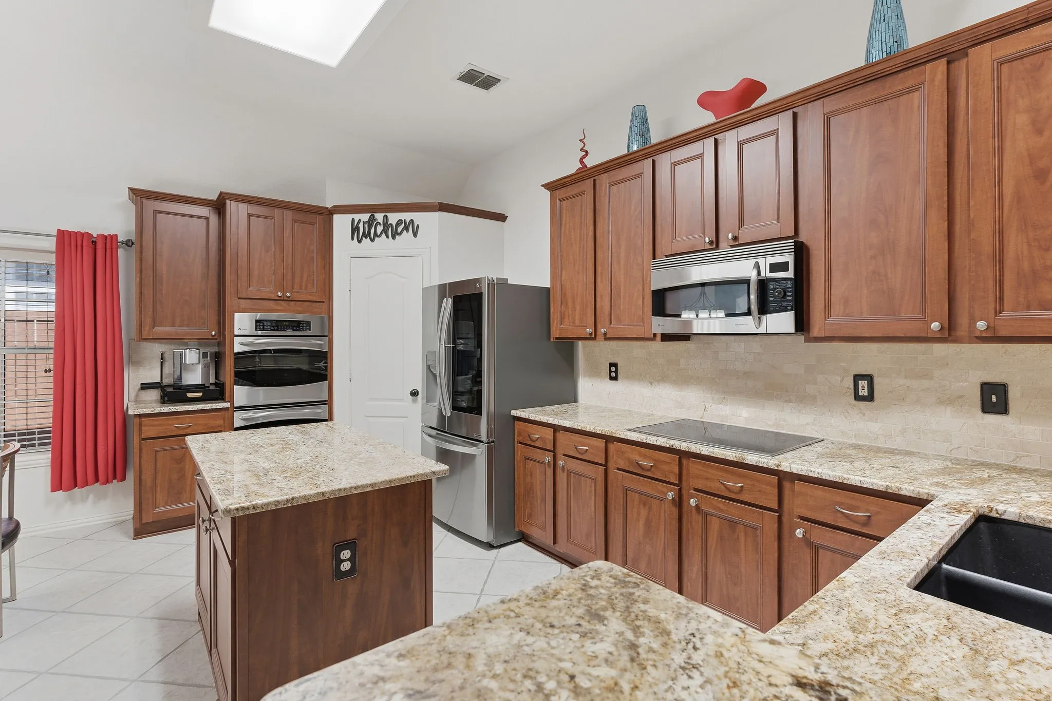 Wood-finish cabinetry, light-toned stone countertops, a full suite of stainless steel appliances, a kitchen island, and a tile floor