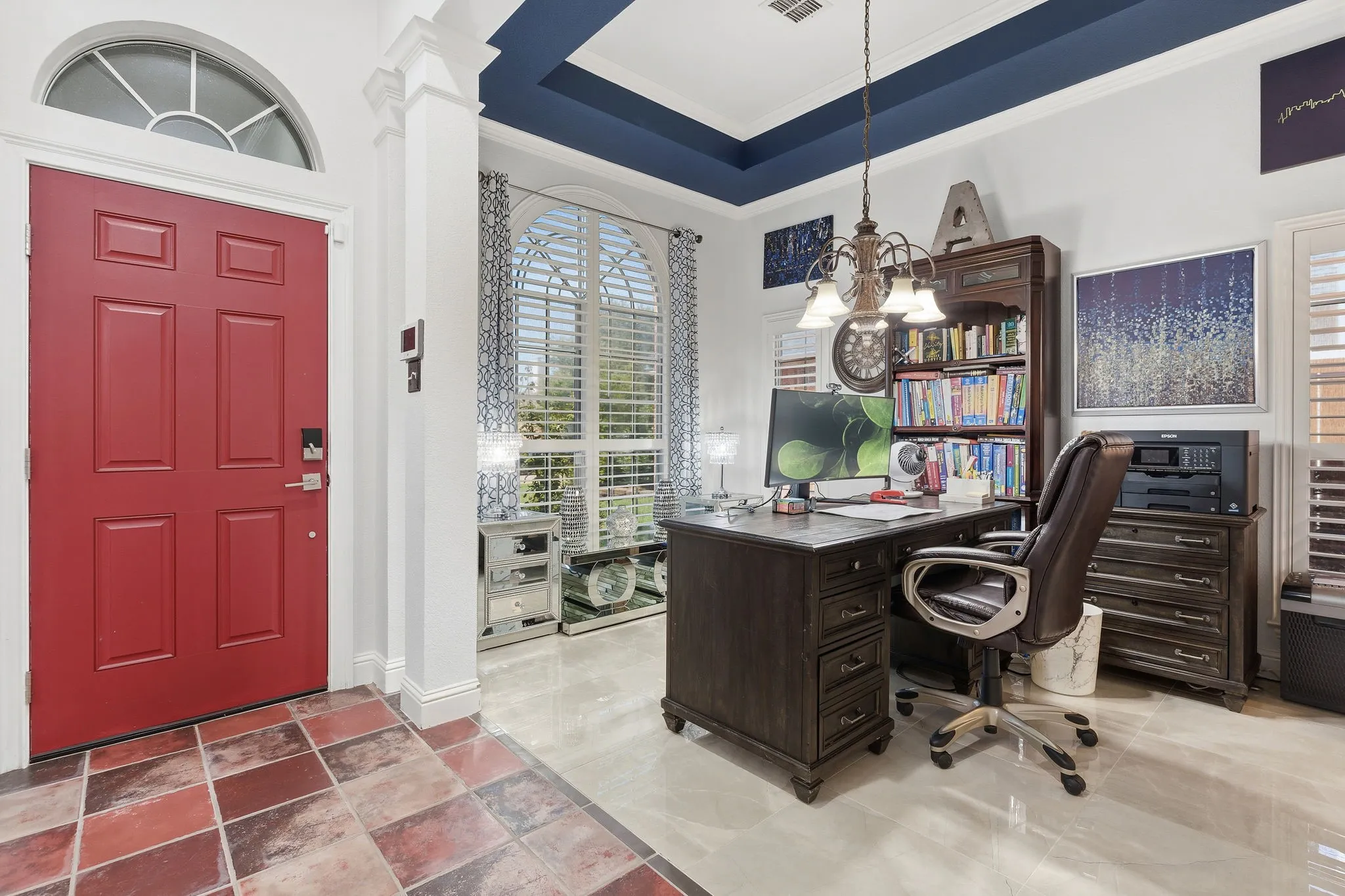 Red panel door with an arched transom window, leading to a space with a tray ceiling and a chandelier