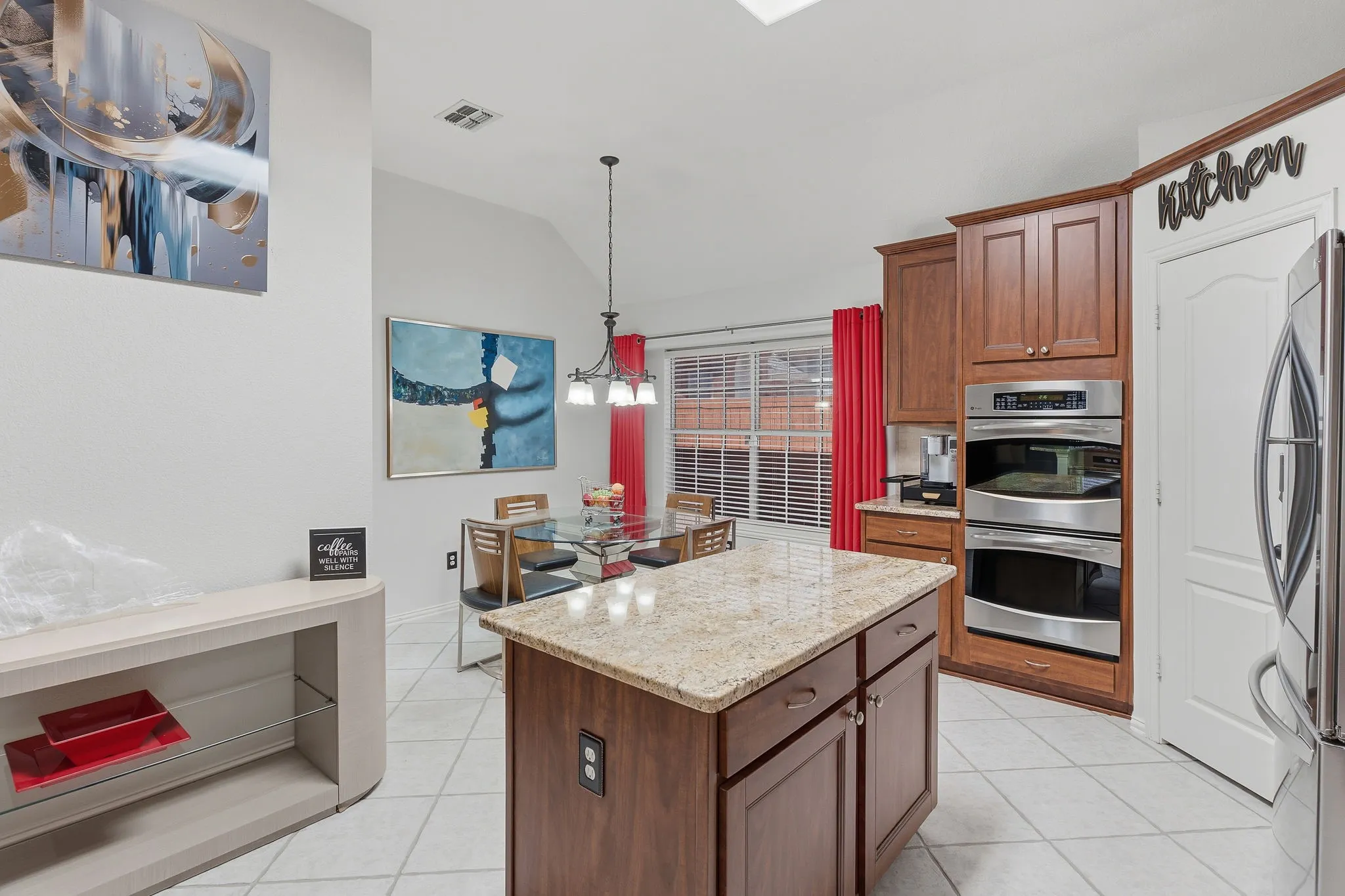 Kitchen island with granite countertop, wood cabinetry, stainless steel double oven, and tiled flooring