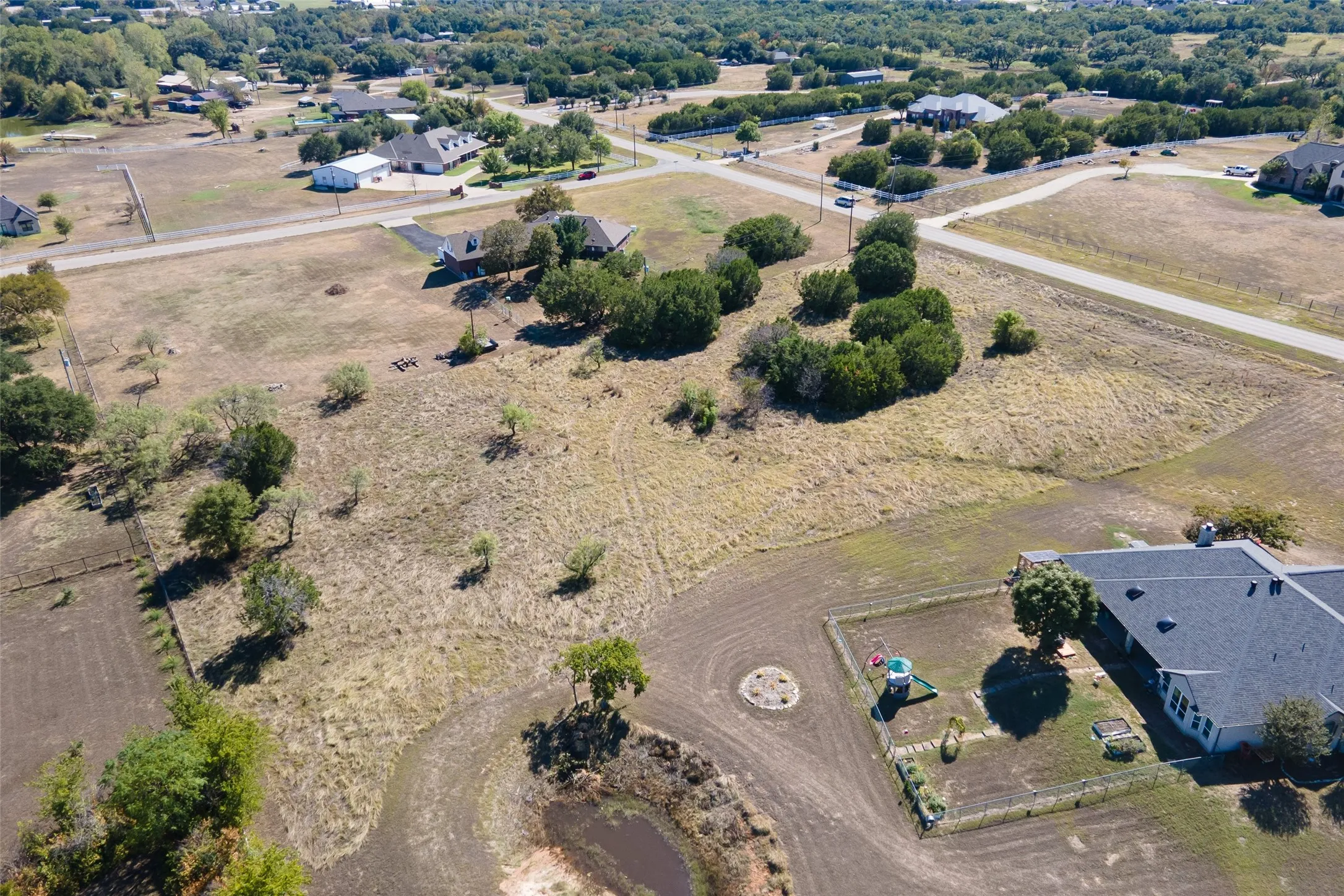 Expansive lot featuring a natural pond, scattered mature trees, and a gravel driveway