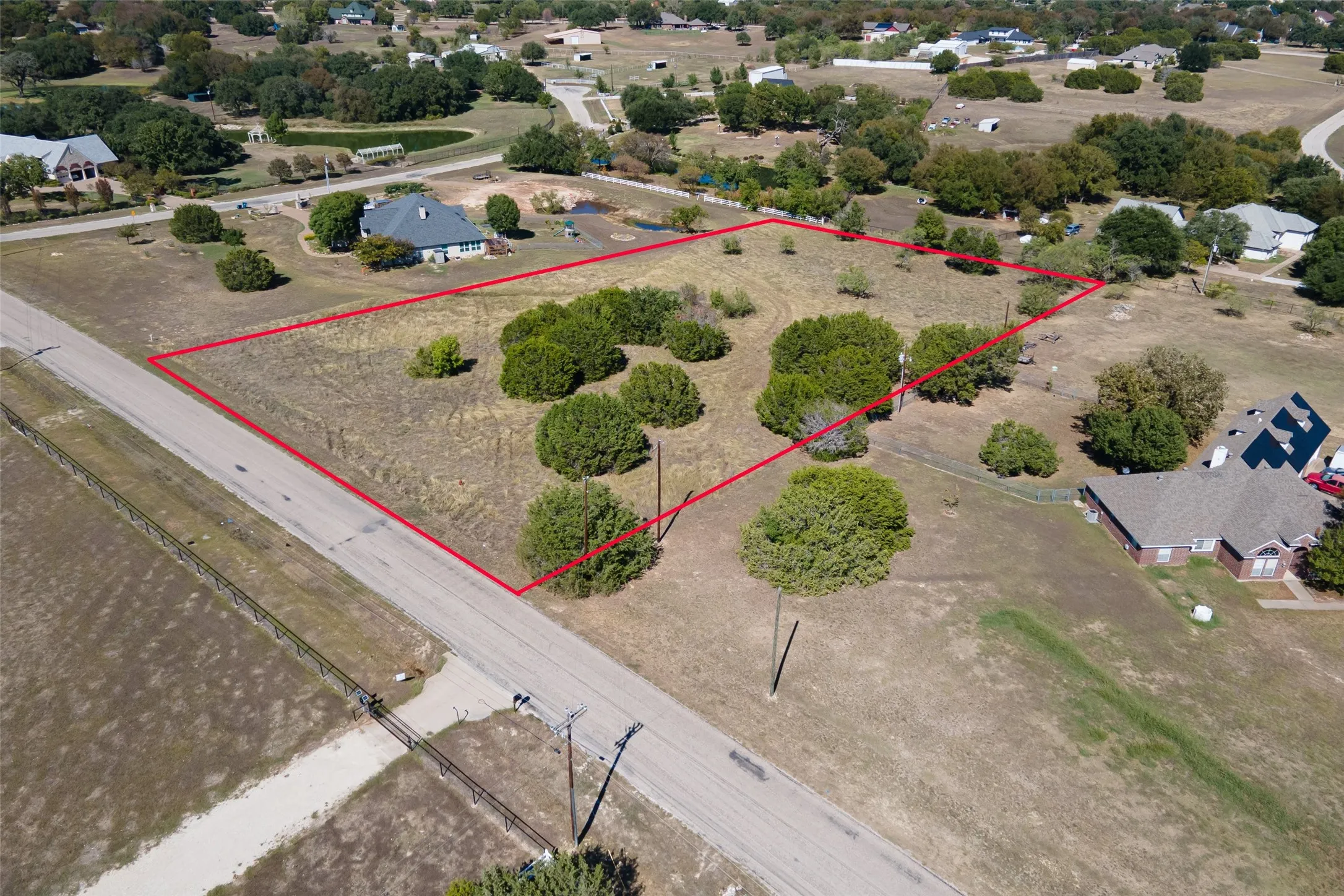 Expansive parcel featuring a paved road frontage, mature trees, and open land
