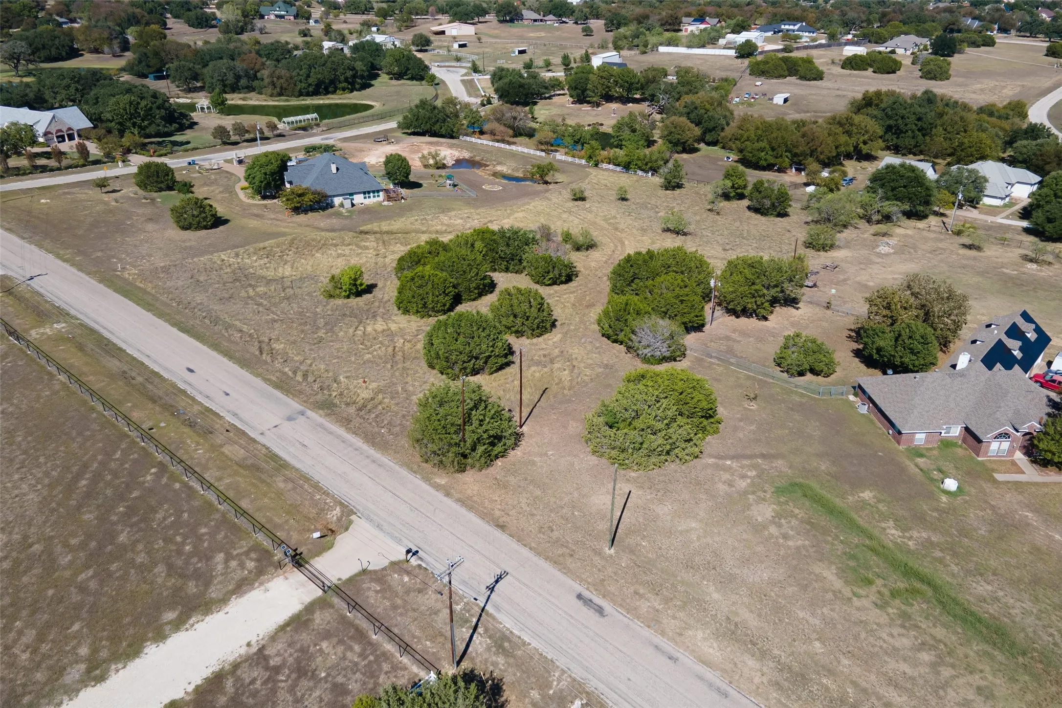 Expansive undeveloped land featuring a paved road, scattered mature trees, and a perimeter fence