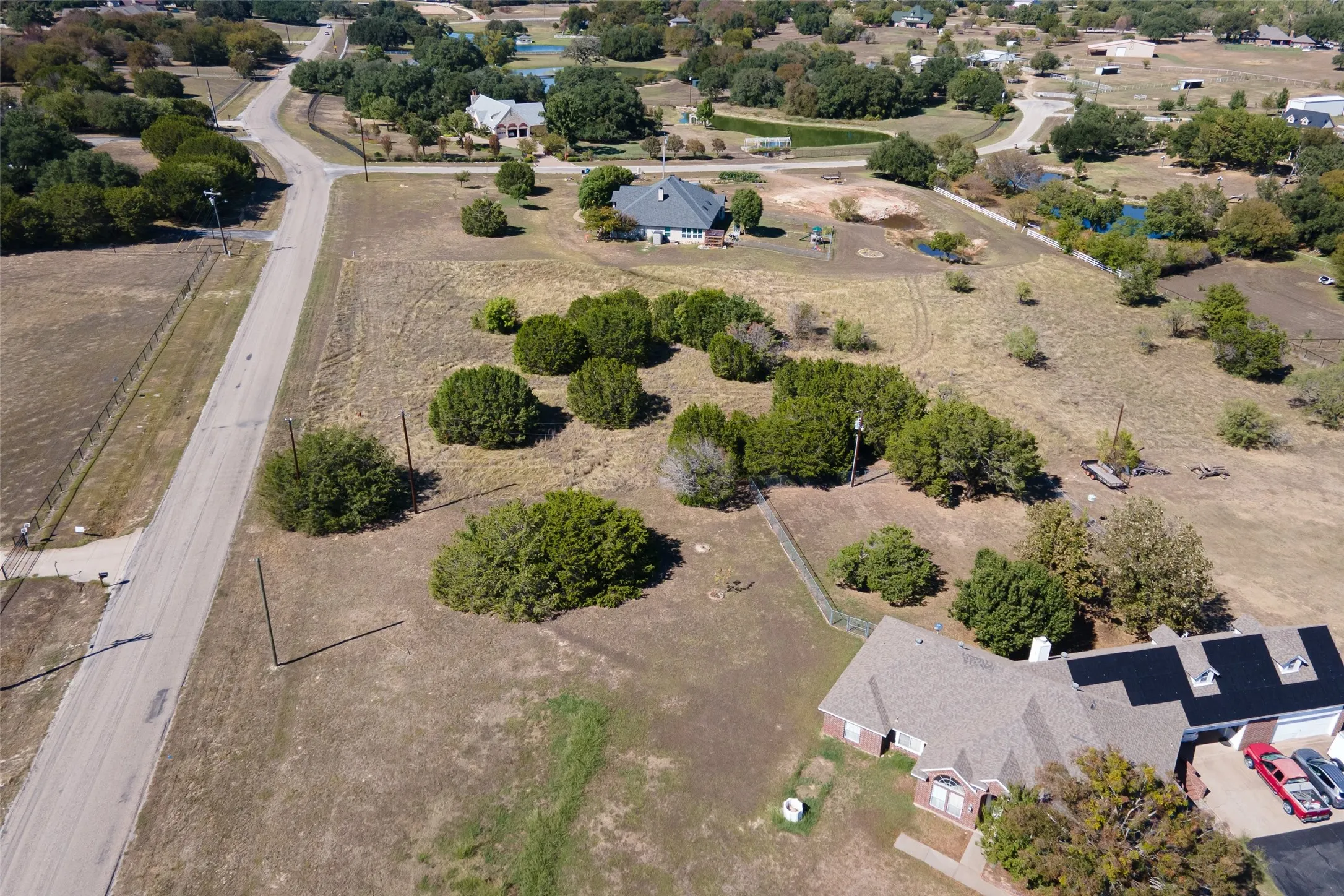 Expansive lot featuring a paved road, scattered trees, and a distant body of water