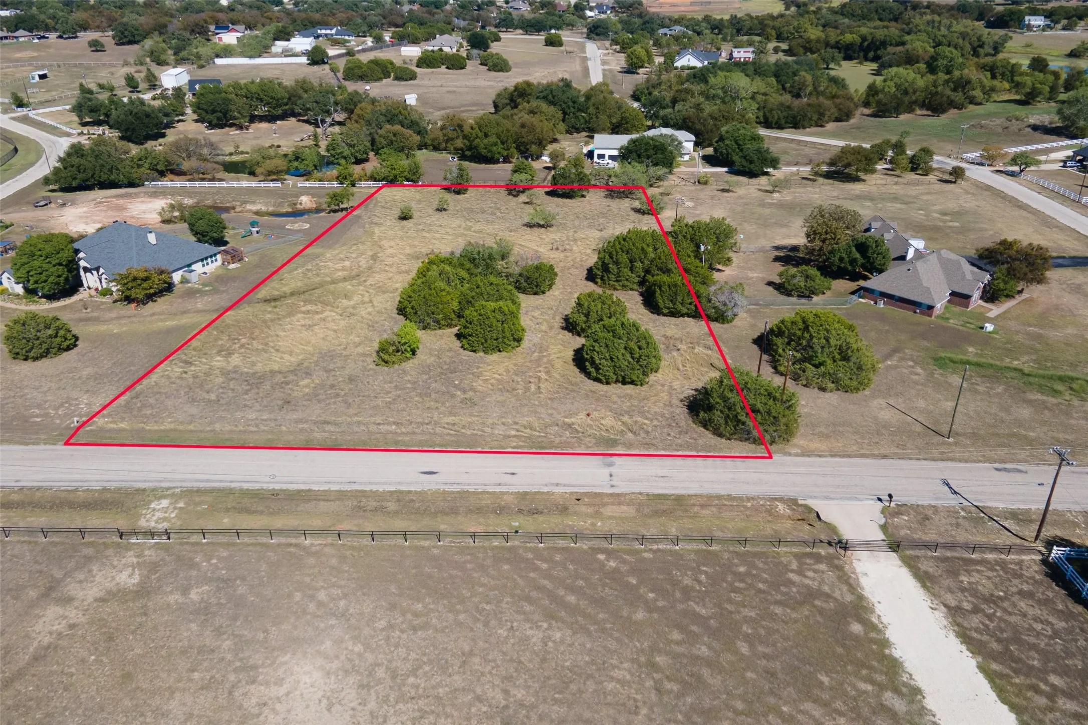 Expansive land lot featuring mature trees and a paved road frontage