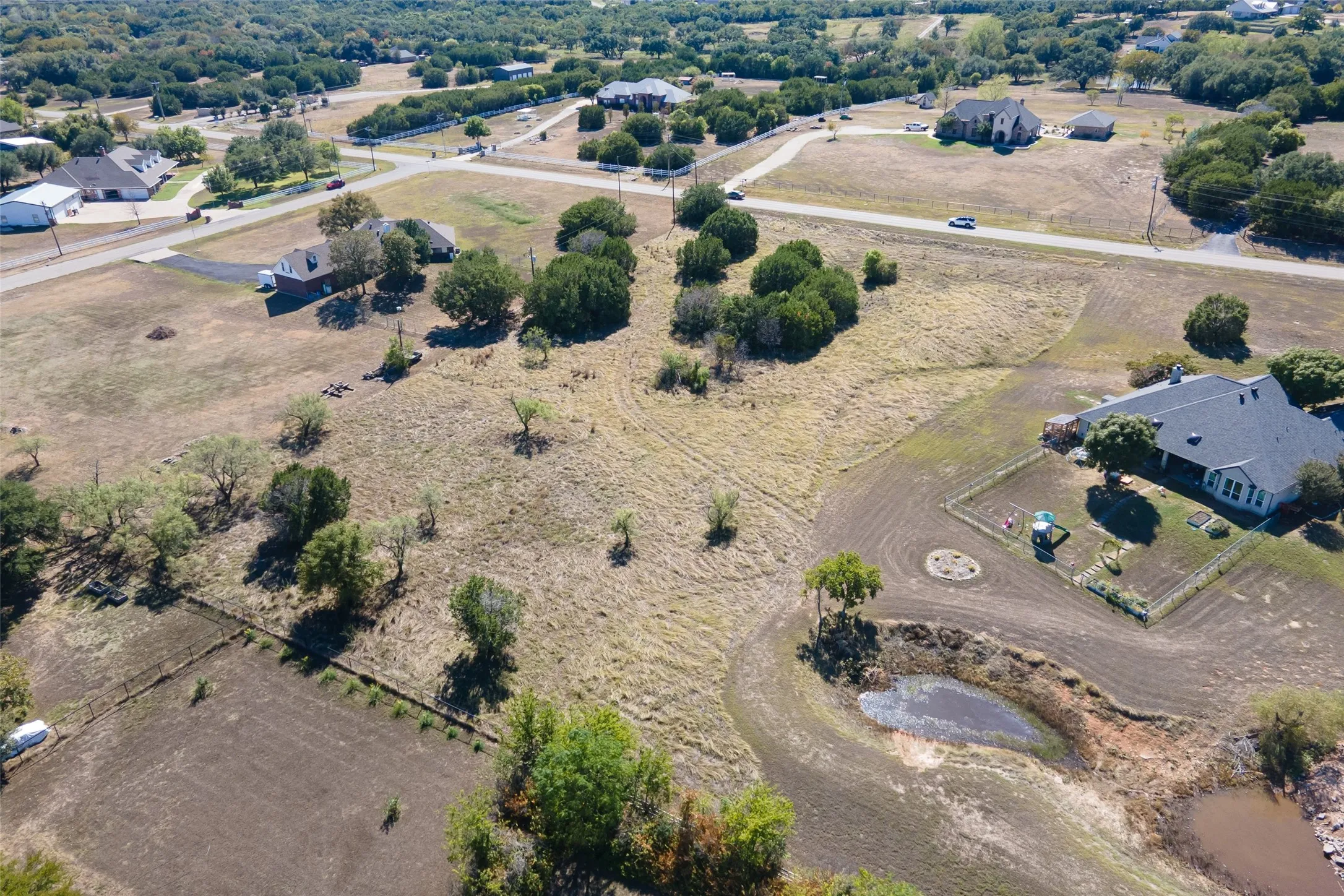Expansive lot featuring a natural pond, scattered trees, and surrounding roads