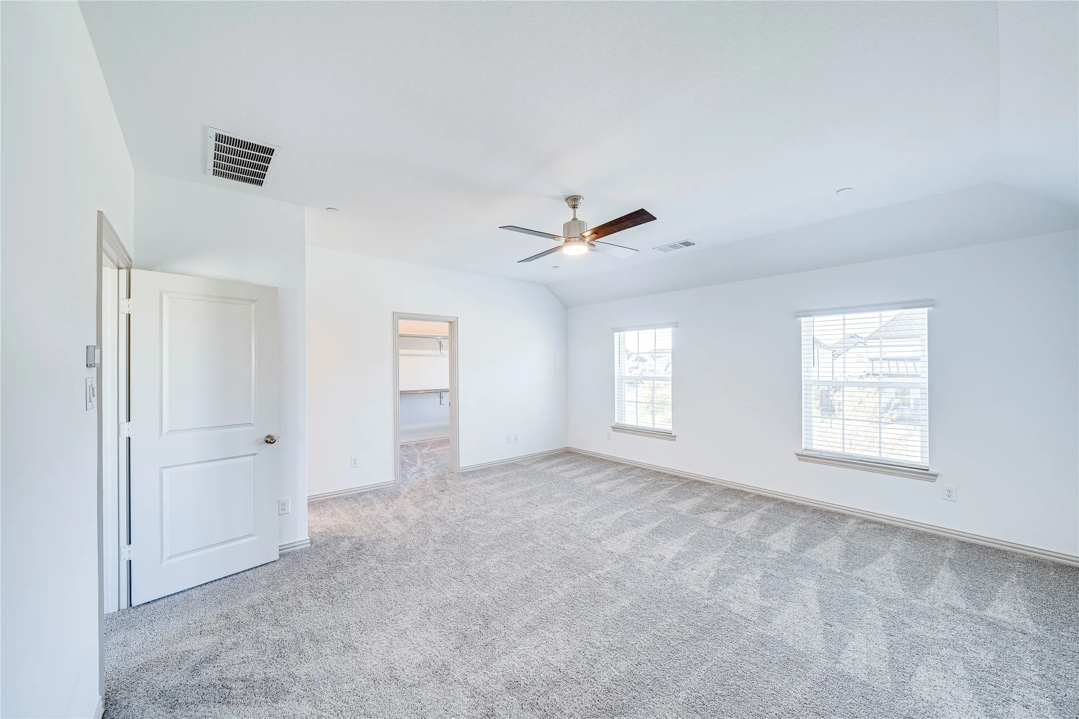 Spacious room featuring neutral carpeting, a ceiling fan, and two windows with blinds