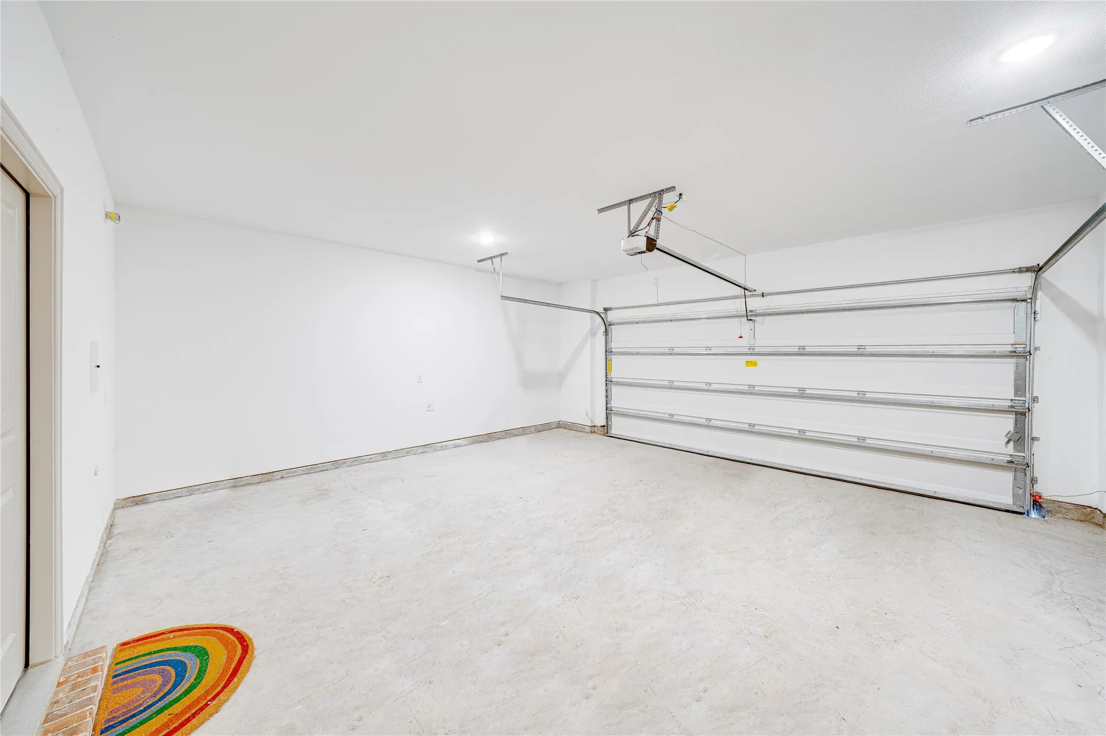 Attached garage with a white sectional door, concrete flooring, and overhead lighting
