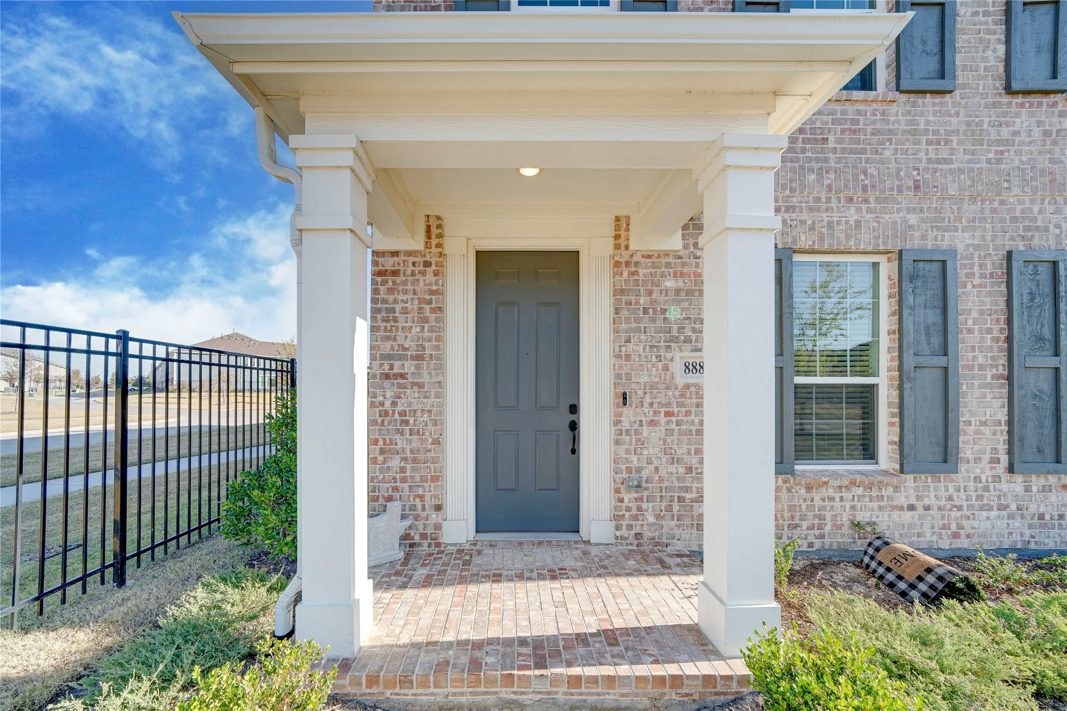 Brick exterior with a covered entry, decorative shutters, and an iron fence