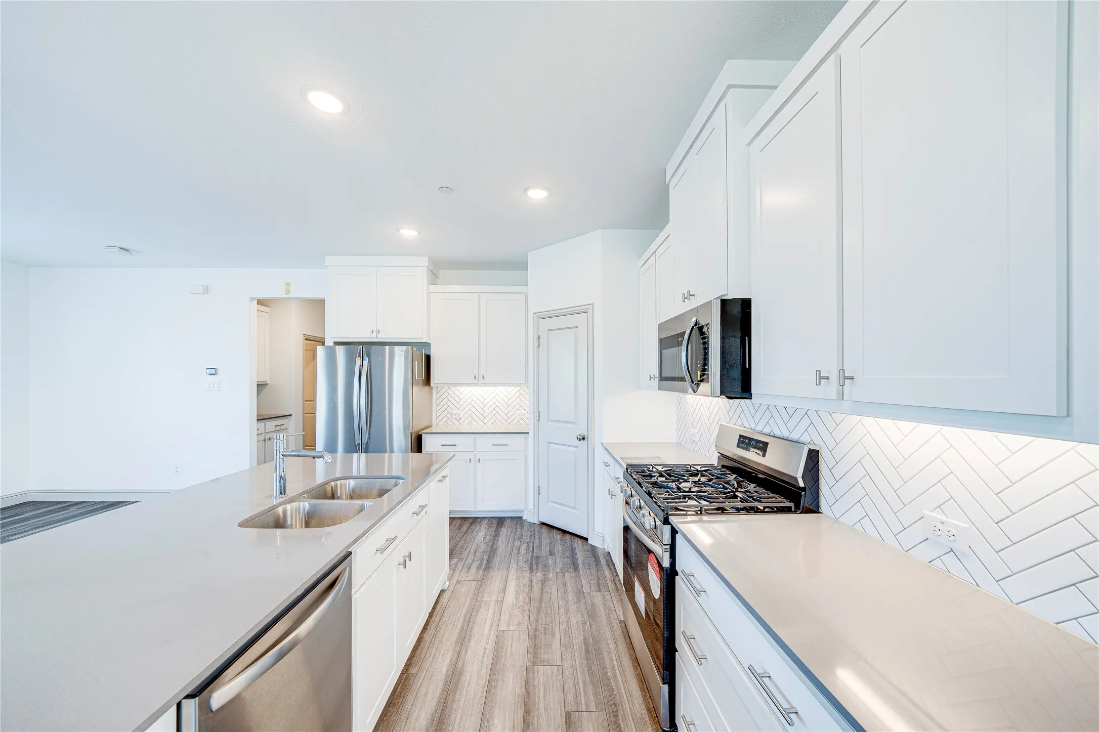 Modern kitchen featuring white cabinetry, stainless steel appliances, light countertops, a herringbone tile backsplash, and wood-finish flooring