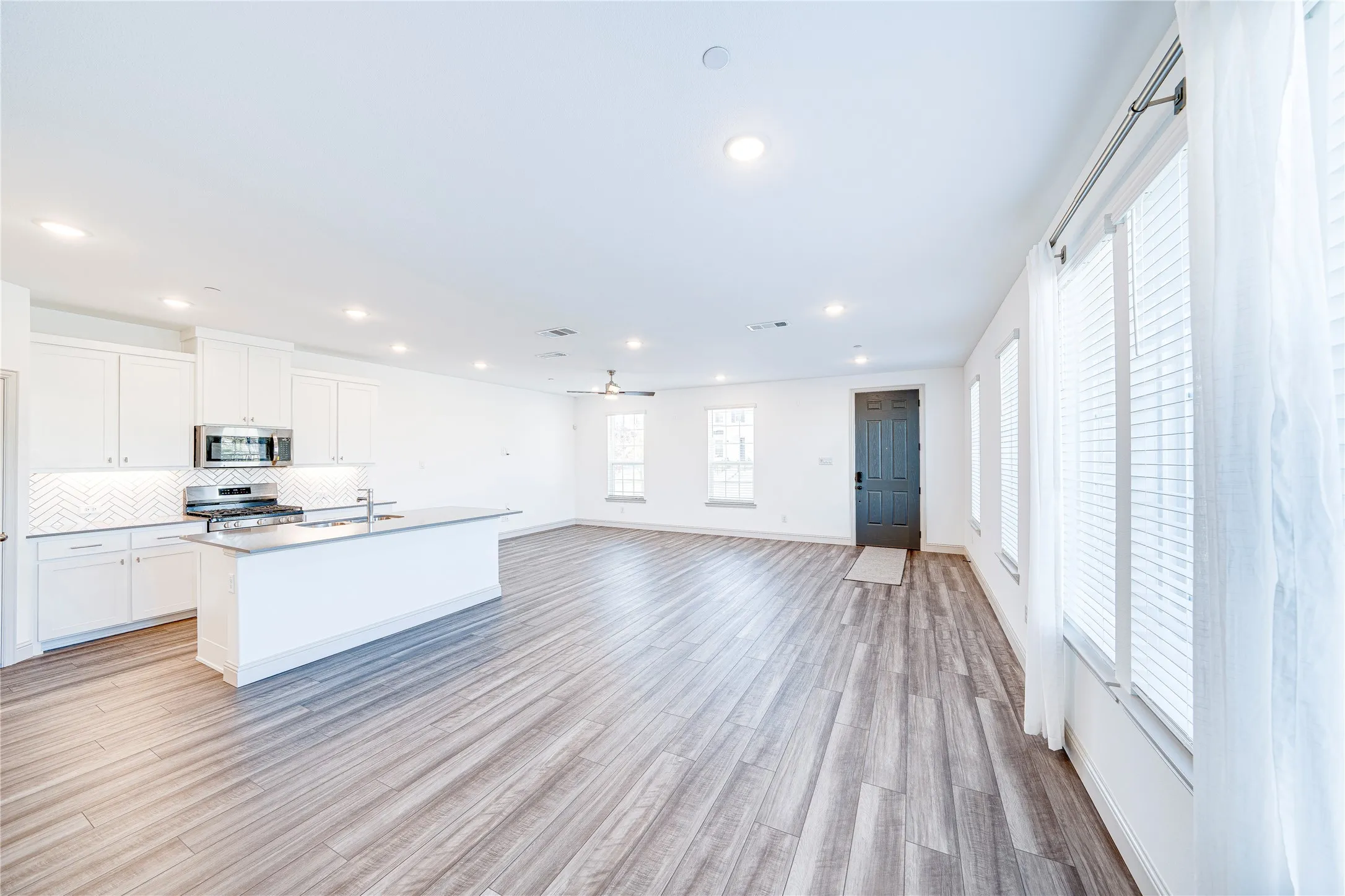 Open-concept living area featuring wood-finish flooring, recessed lighting, and multiple windows with blinds