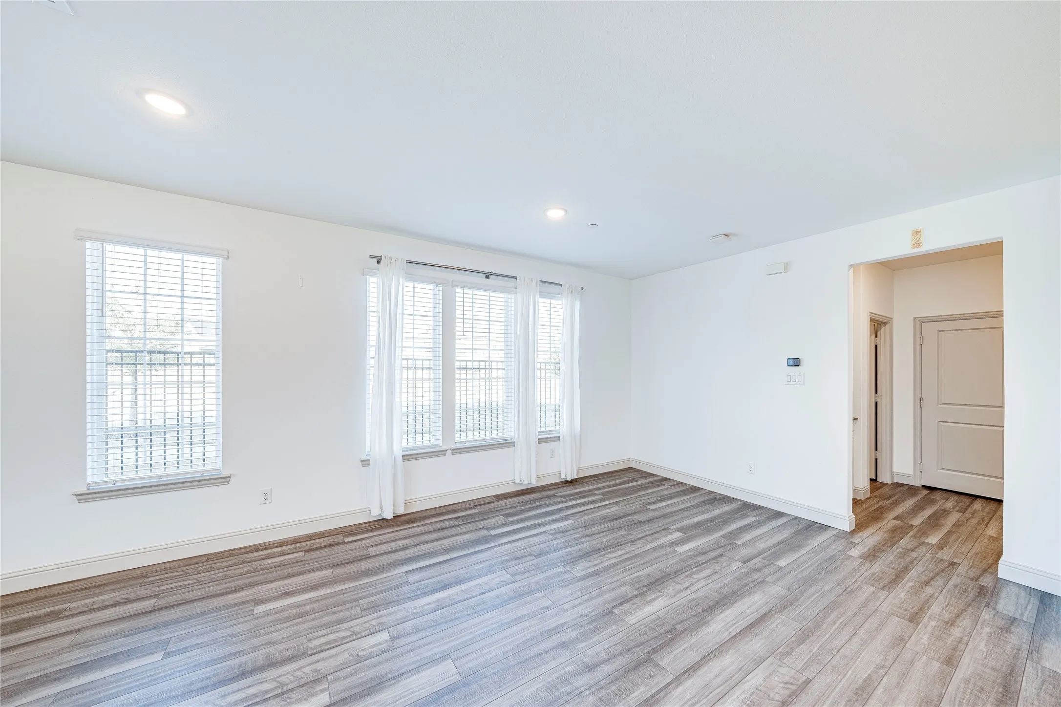 Spacious room featuring wood-finish flooring, recessed lighting, and multiple windows with blinds