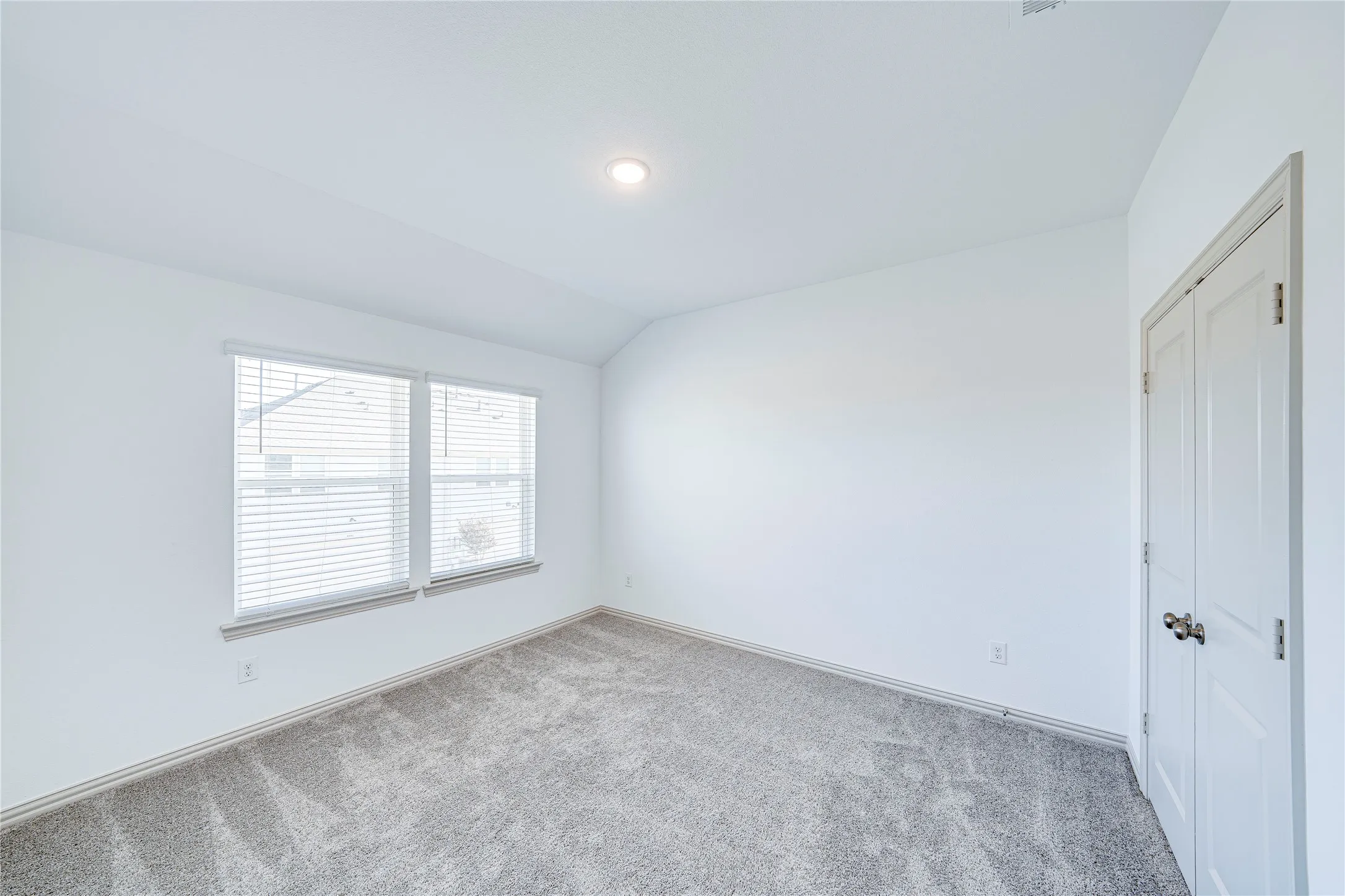 White walls, recessed lighting, and a double window with blinds