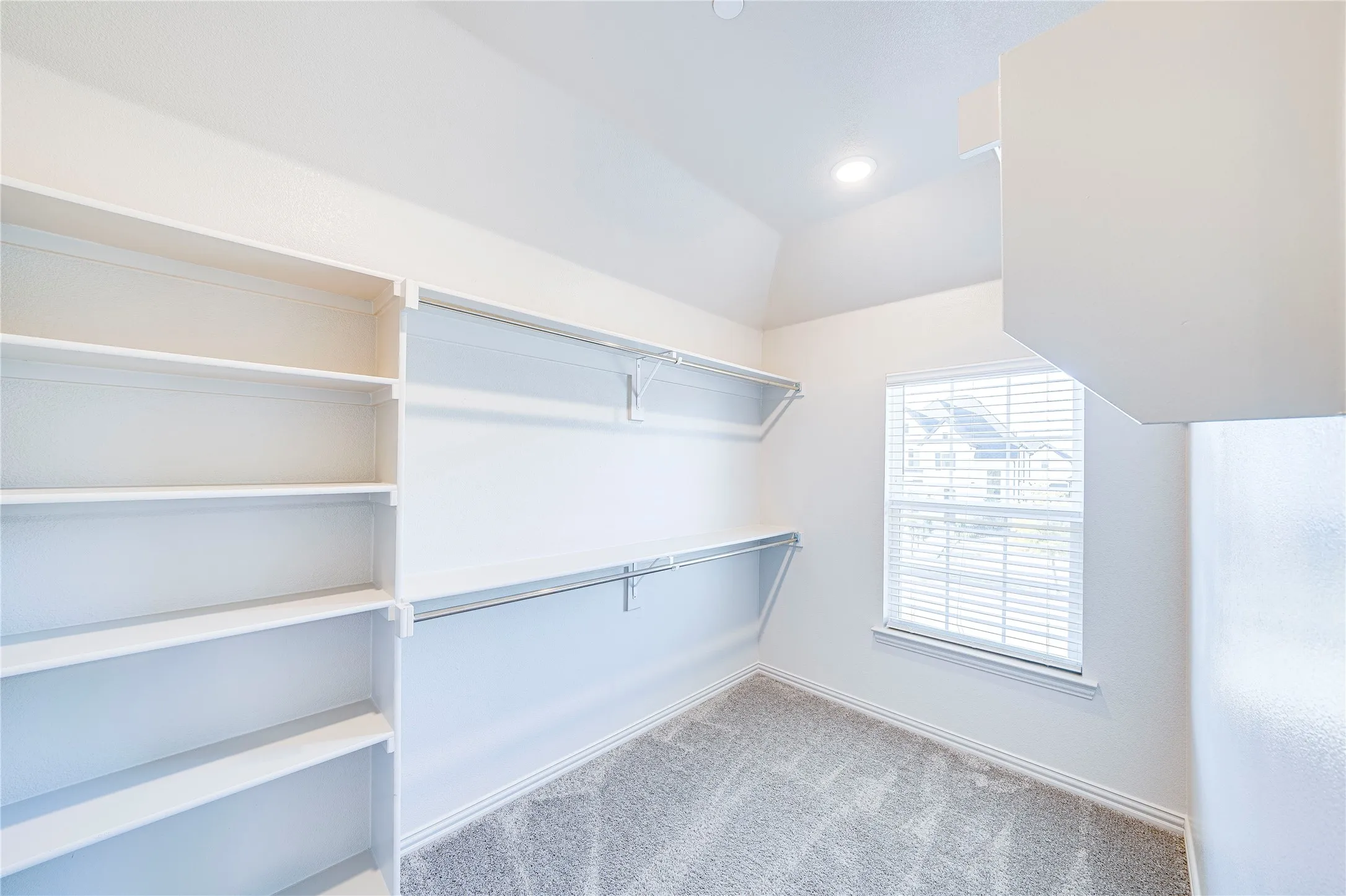 Walk-in closet with built-in shelving, hanging rods, and a window with blinds