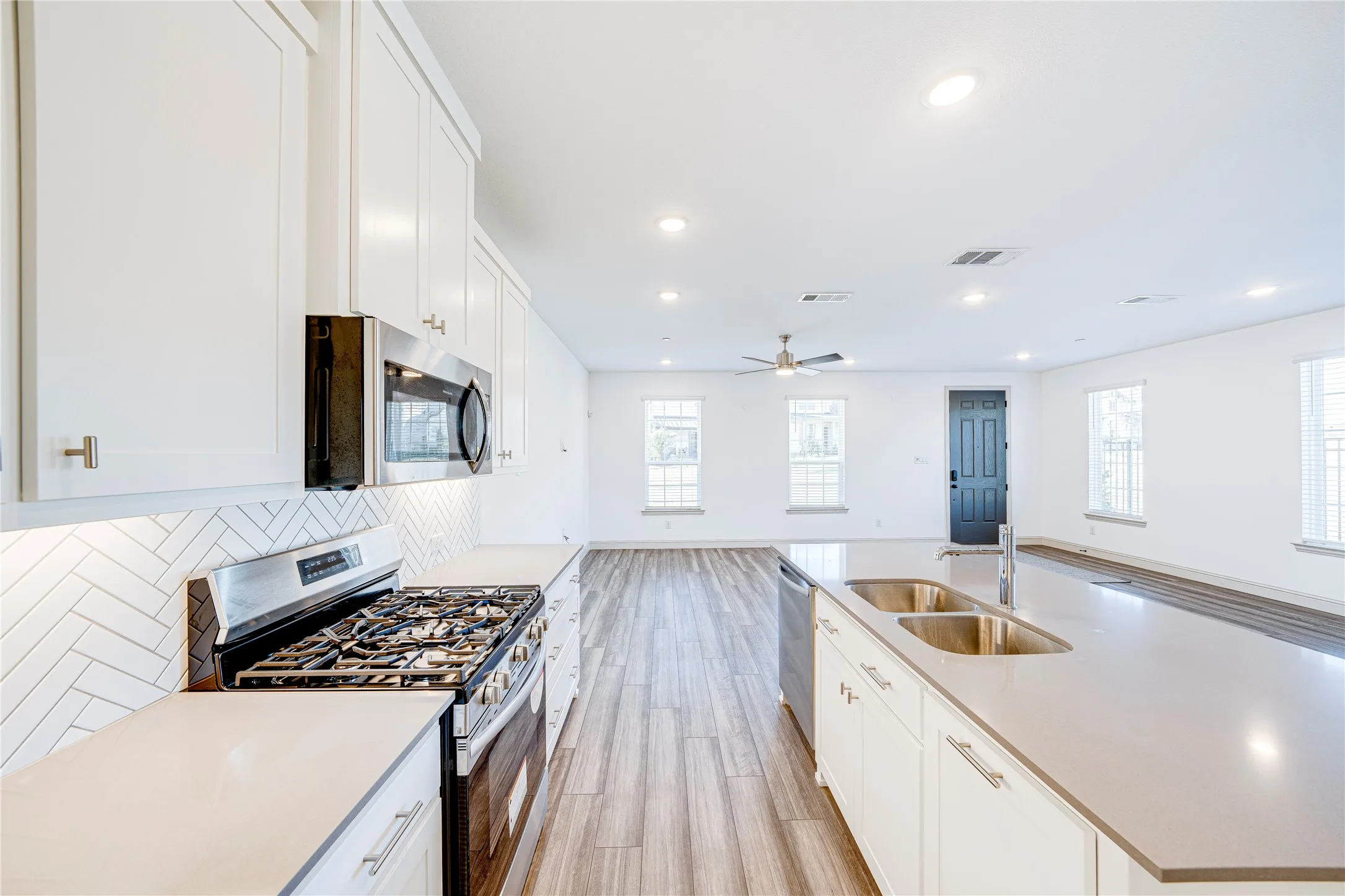 Sleek kitchen featuring white cabinetry, stainless steel appliances, a herringbone tile backsplash, and an expansive island with dual sinks