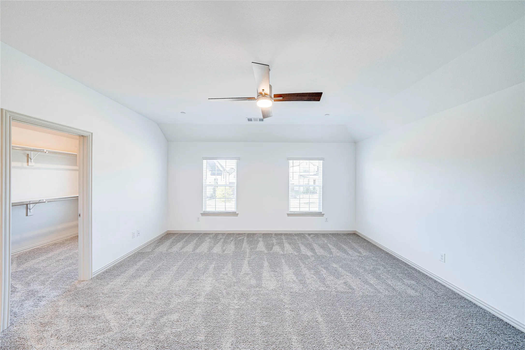 Spacious room featuring vaulted ceilings, light gray carpeting, two windows, and a ceiling fan