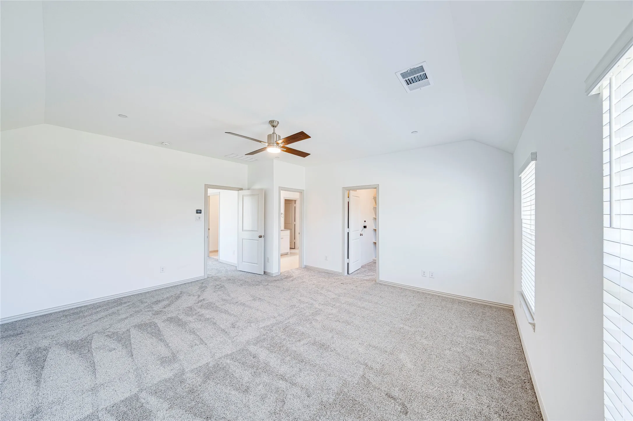 Vaulted ceiling with a contemporary ceiling fan, light-toned carpeting, multiple windows with blinds, and white interior doors
