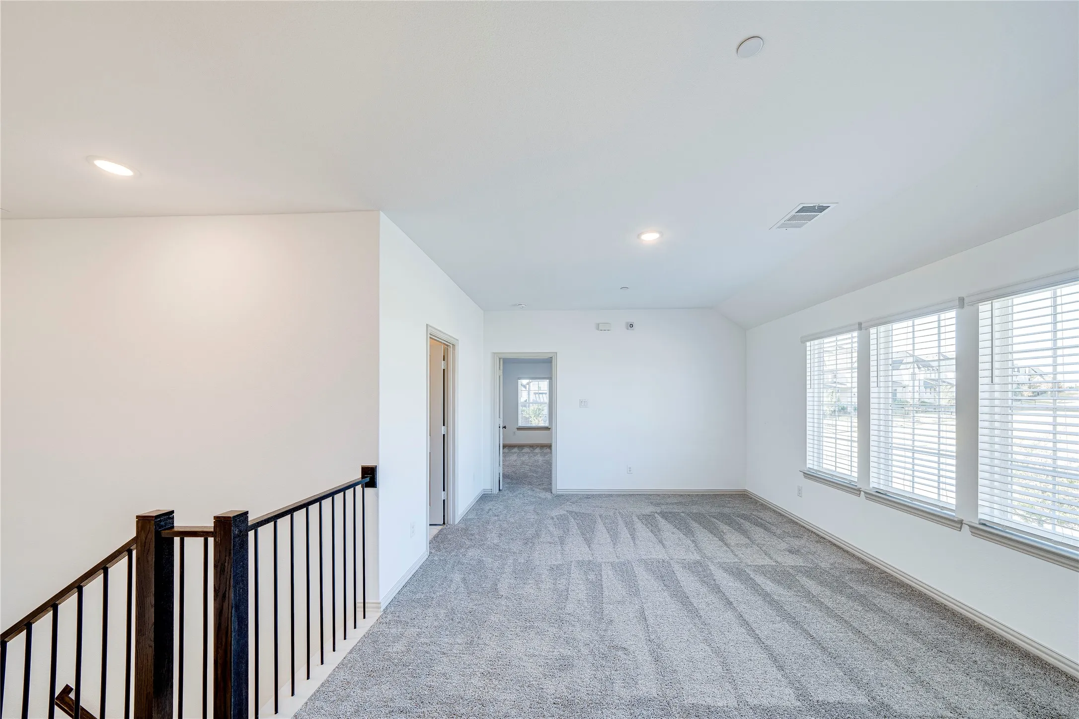 Carpeted room with multiple windows, recessed lighting, and a balustrade