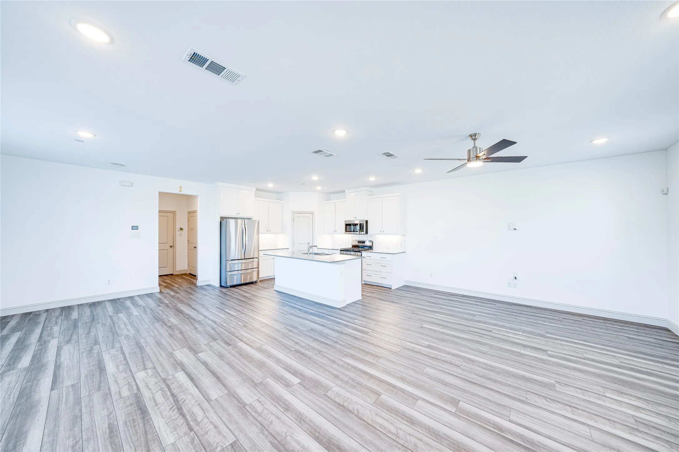 Open-concept living space featuring wood-finish flooring, recessed lighting, a modern ceiling fan, and a kitchen with an island and stainless steel appliances