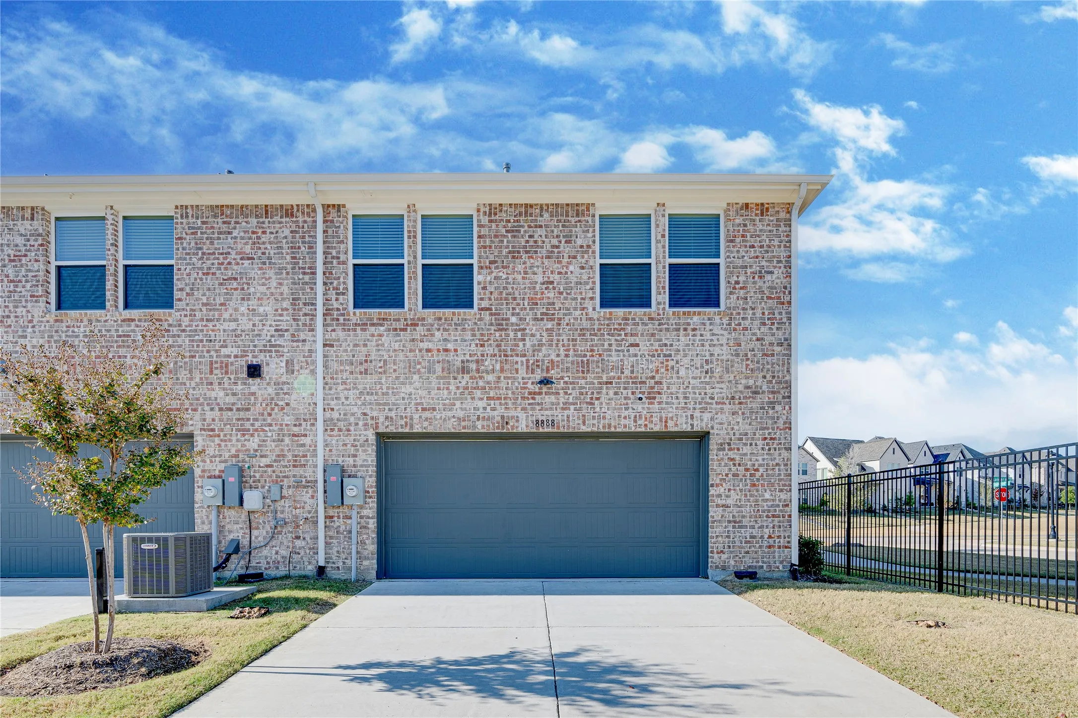 Brick exterior with white window frames, an attached garage, a concrete driveway, and a black metal fence