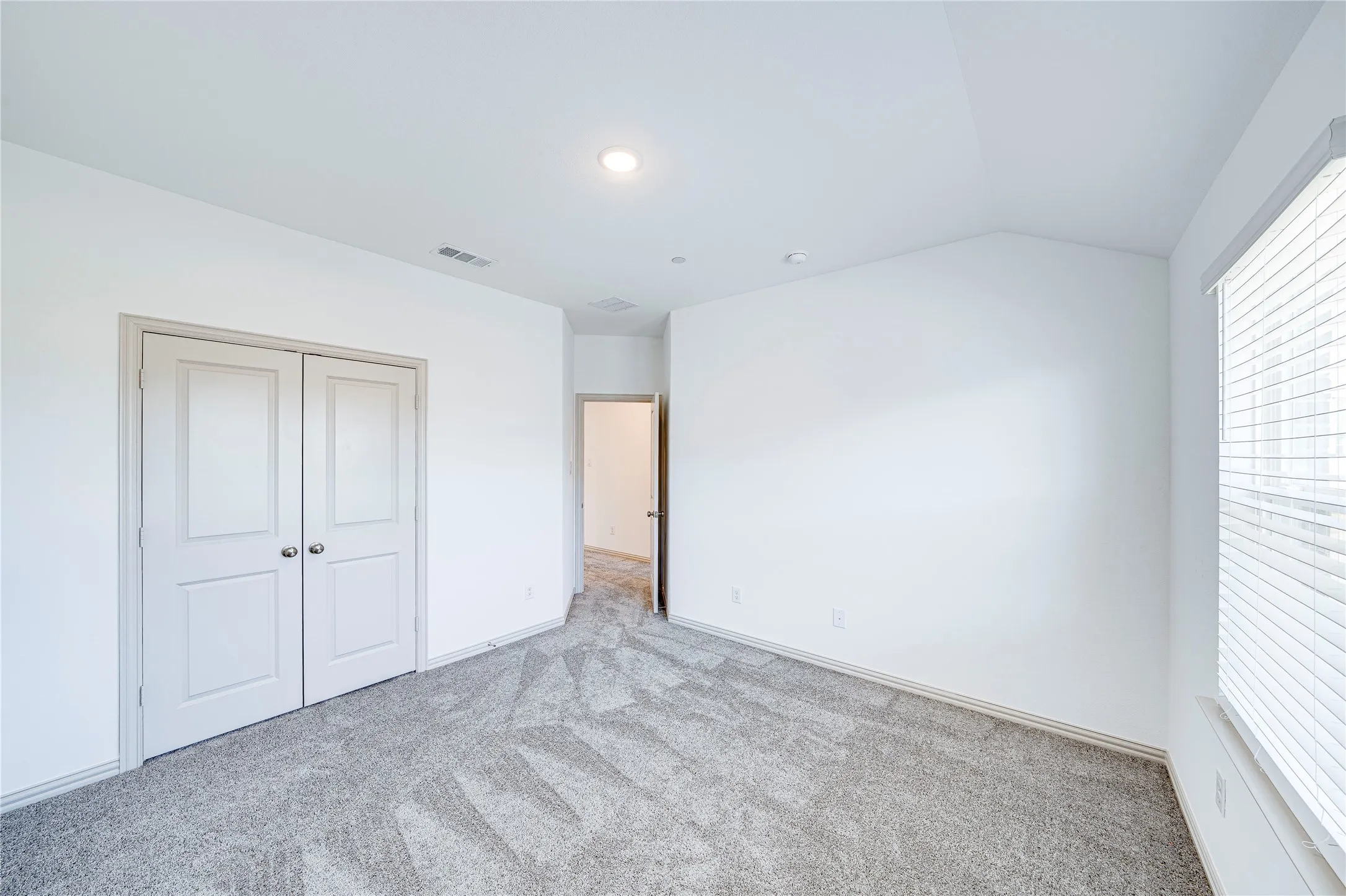 Vaulted ceiling, recessed lighting, double panel doors, neutral carpeting, and a window with blinds