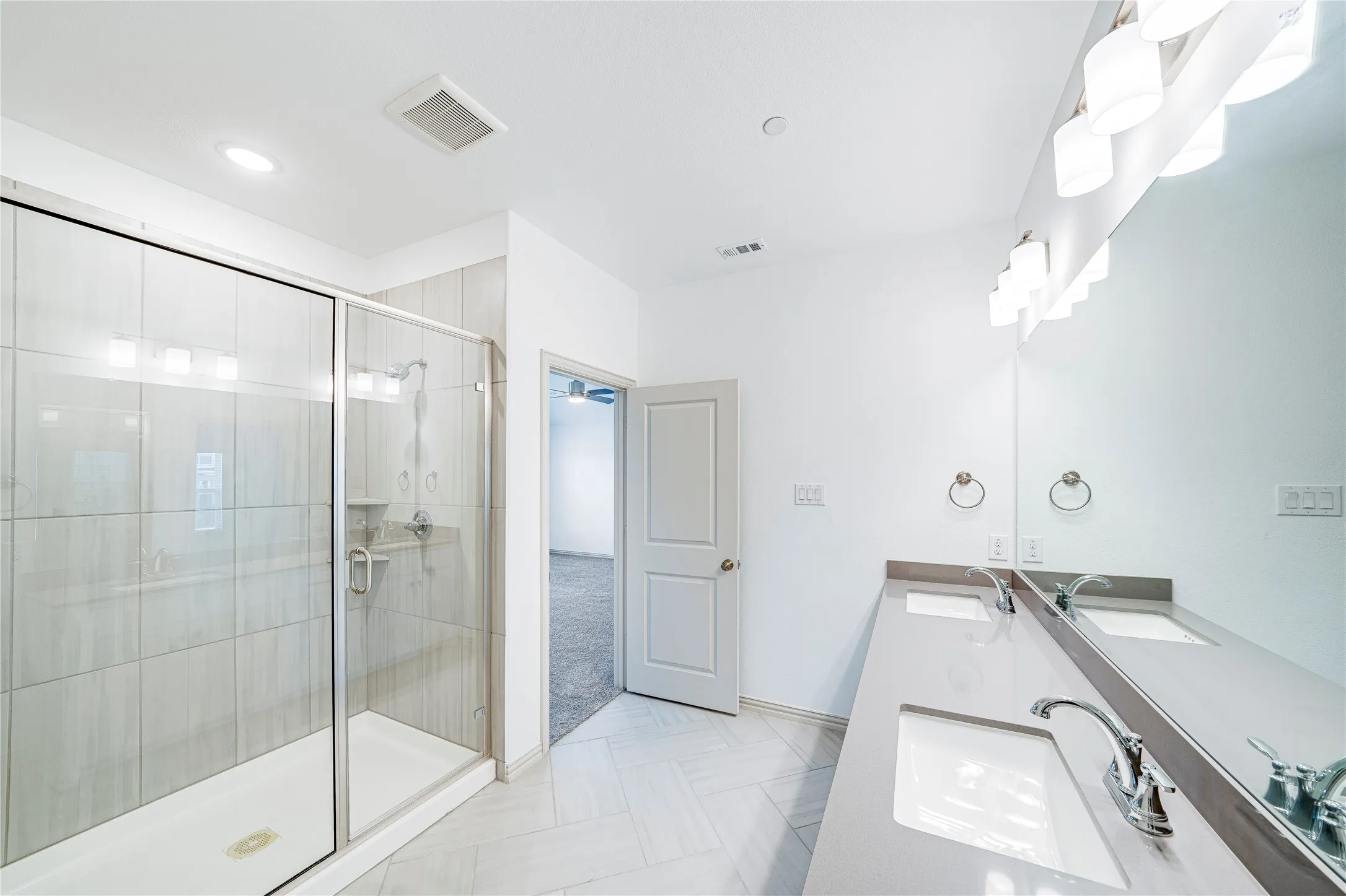 Glass-enclosed shower with subway tile surround, dual vanity with undermount sinks, and a full-width mirror
