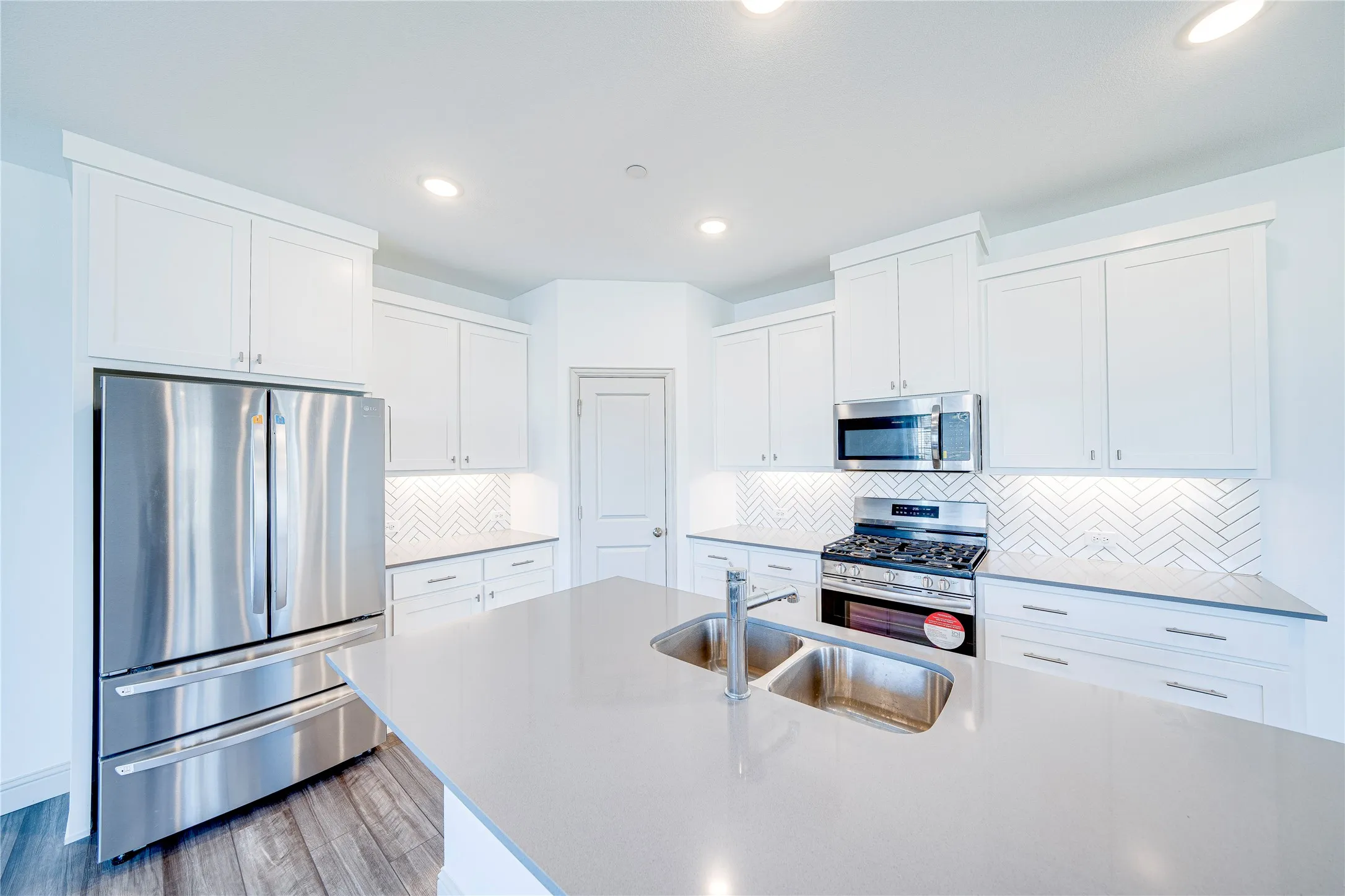 Kitchen featuring a large island with an undermount double-basin sink, stainless steel appliances, white cabinetry, herringbone tile backsplash, and recessed lighting
