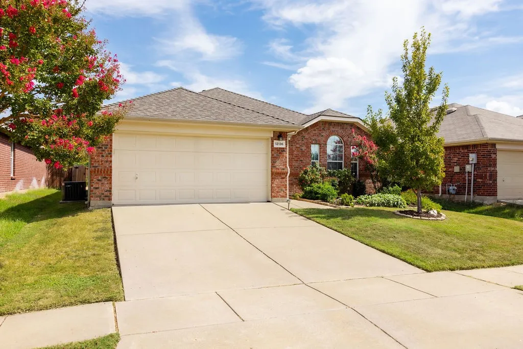 Brick-clad exterior with an arched window, attached garage, concrete driveway, and established landscaping
