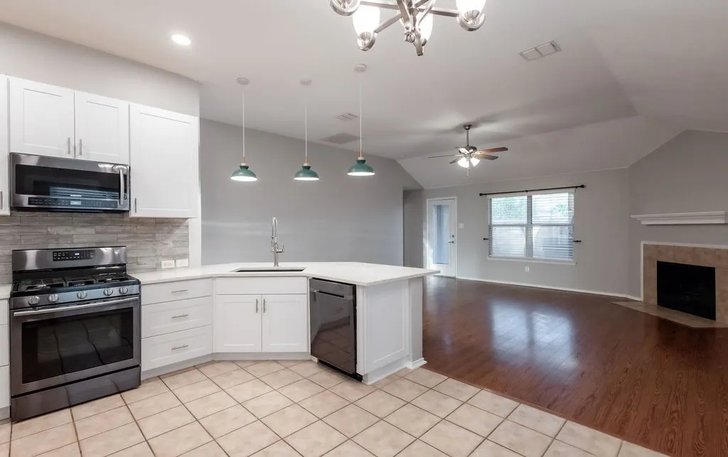 White cabinetry with stainless steel appliances, white countertops, tile flooring, wood-finish flooring, and a fireplace with a stone surround