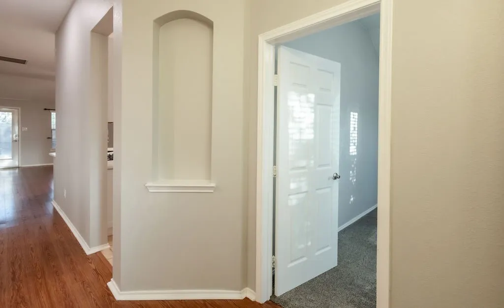 Hallway with wood-finish flooring, recessed wall niche, and white trim molding