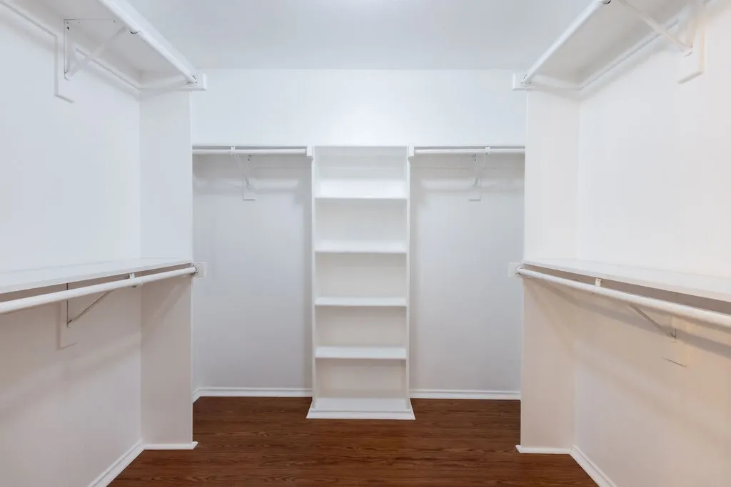 Walk-in closet with ample shelving and hanging rods, featuring wood-finish flooring