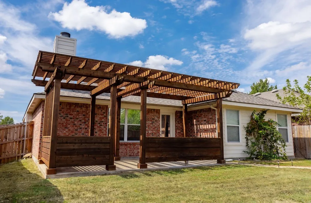 Expansive wood pergola with partial privacy screen, brick exterior accent, concrete patio, and fenced backyard