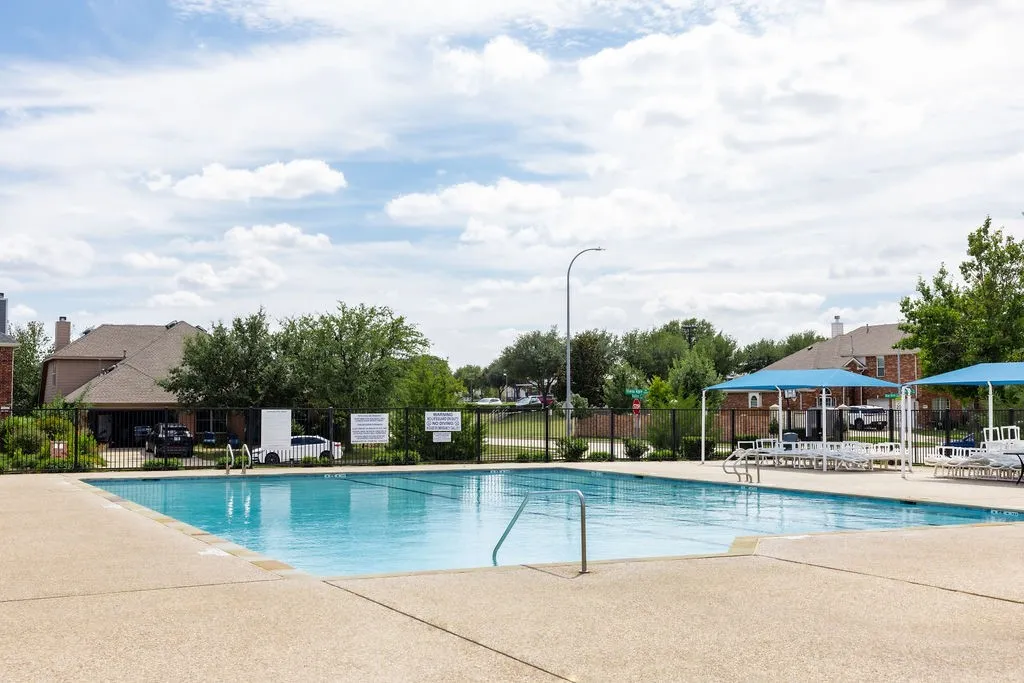 Community swimming pool with surrounding fencing, concrete pool deck, and shaded lounge areas