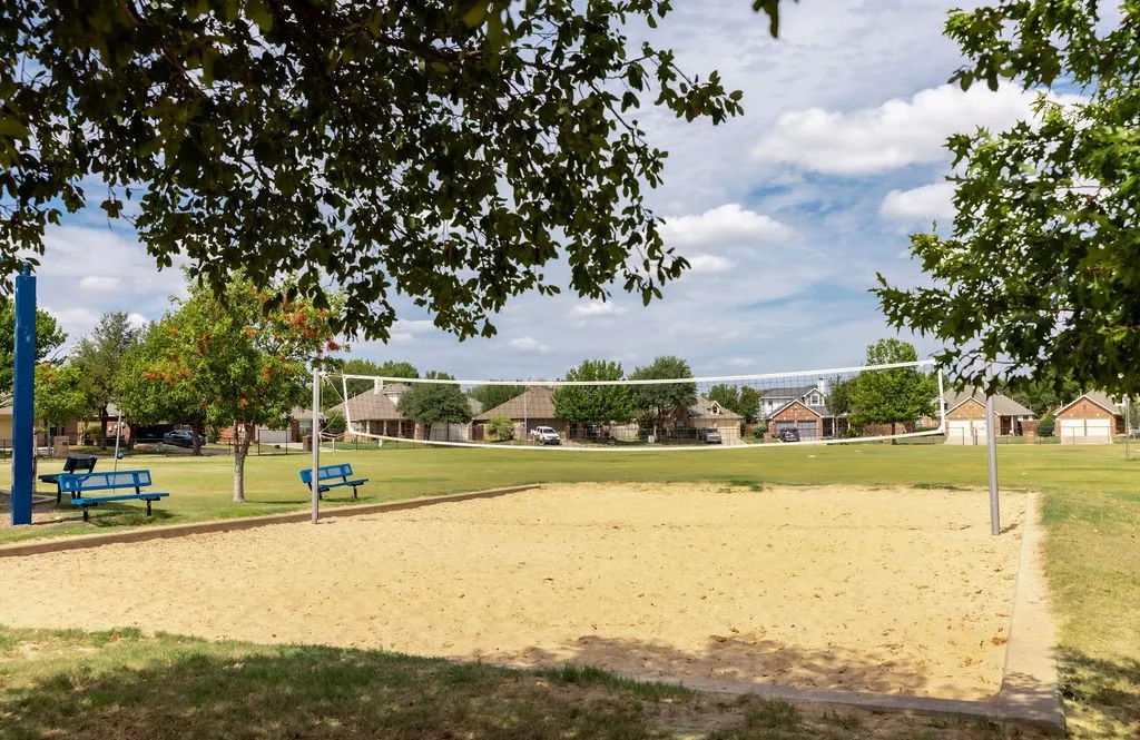Sand volleyball court with a net, bordered by green lawn and mature trees