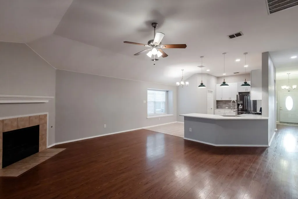 Vaulted ceiling, wood-finish flooring, tiled fireplace, kitchen island with built-in sink, and pendant lighting