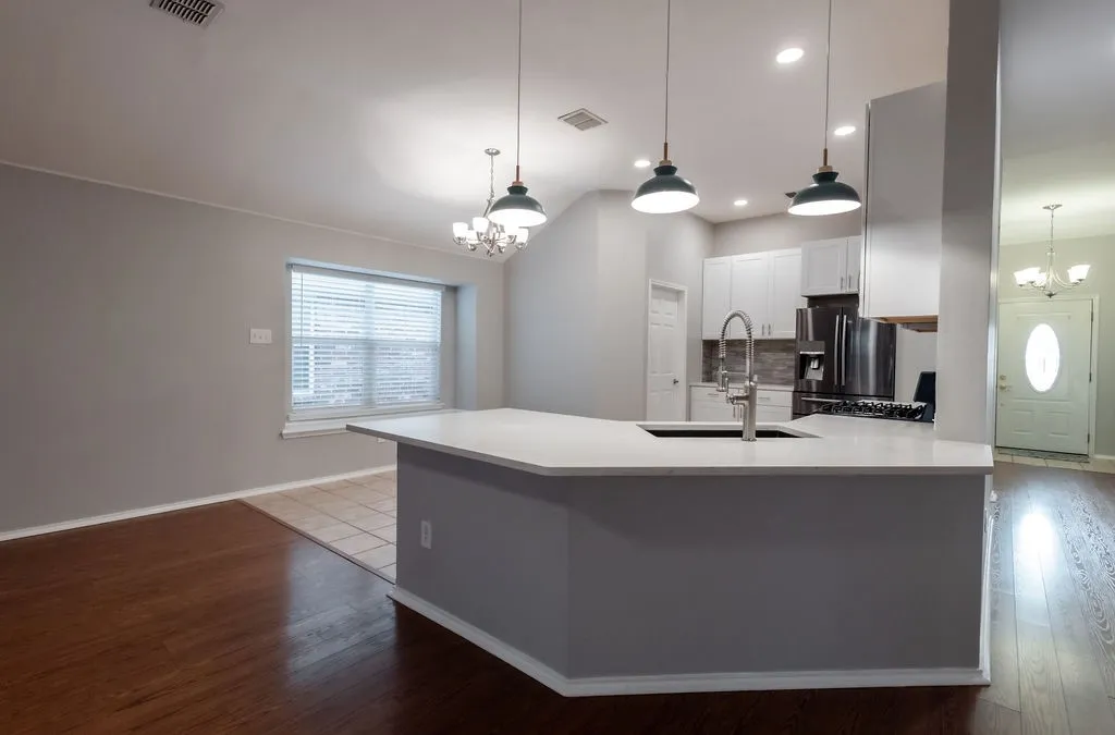 Expansive kitchen island with a light-toned countertop, integrated sink, and contemporary pendant lighting